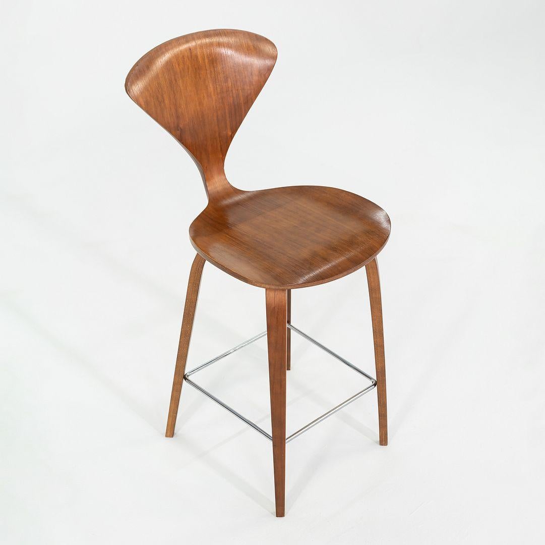 This is a Wood Leg Stool, originally designed by Norman Cherner in 1958. This particular example was produced by Cherner in the USA C. 2005. The chair is comprised of a molded plywood shell and laminated wood legs in walnut with a chrome