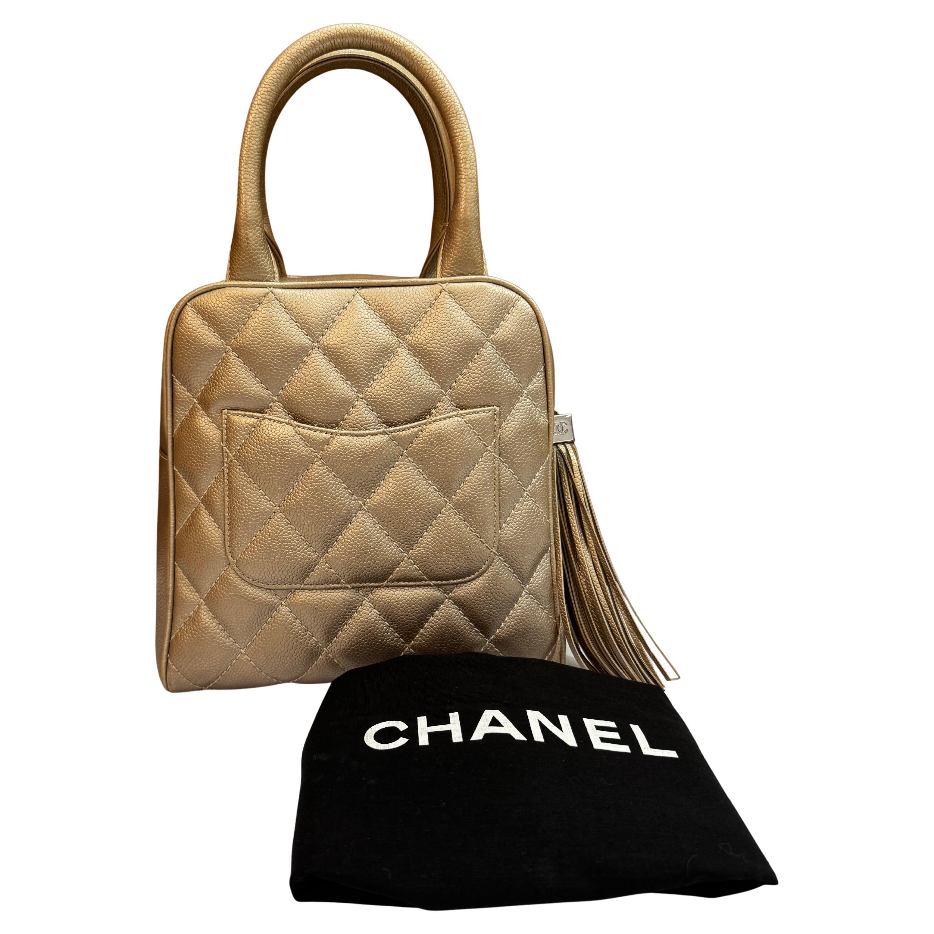 This vintage Chanel small bowler handbag is crafted of diamond quilted caviar calfskin leather in metallic champagne featuring silver toned hardware and a back slip pocket. Top zipper closure with tassel of the same leather opens to a beige fabric
