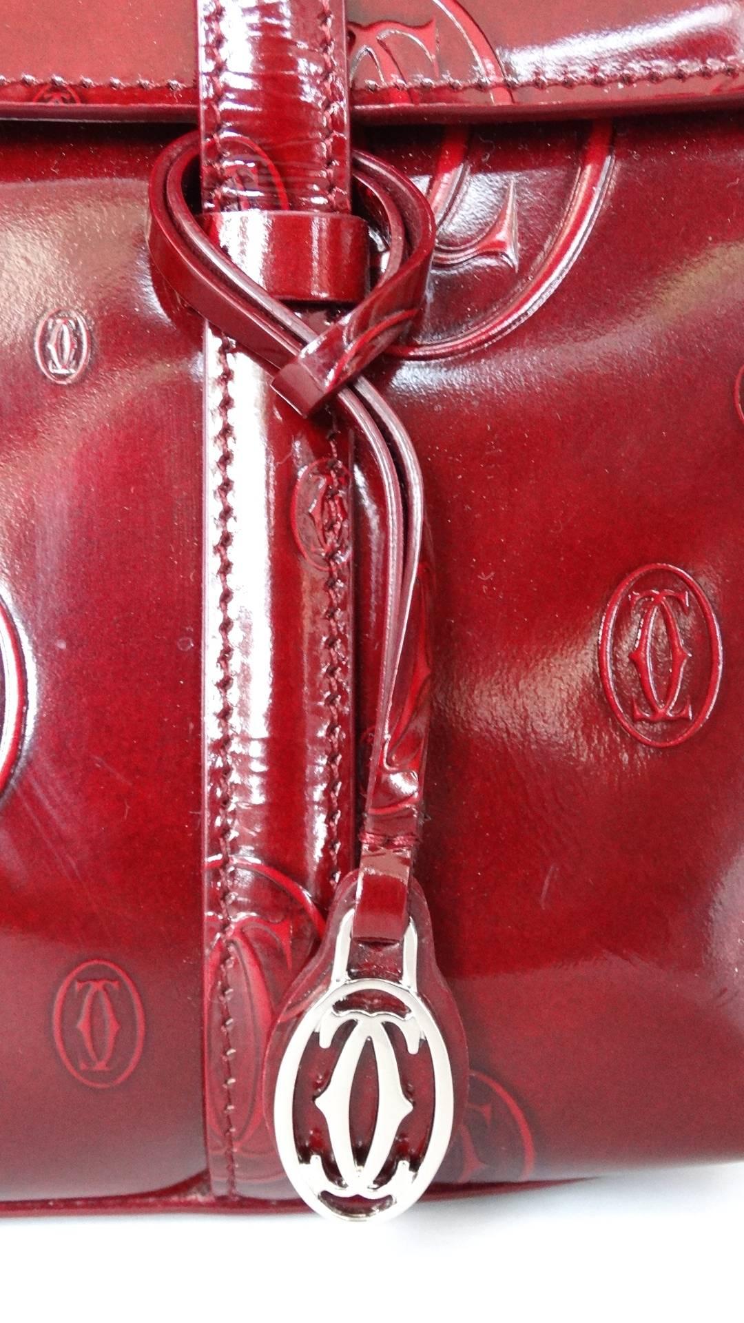 The most adorable Cartier top handle bag from their 2006 Happy Birthday collection! Made of a glossy patent leather in a deep shade of Bordeaux, embossed all over with the Cartier logo. Embellished with a little Cartier charm knotted around the