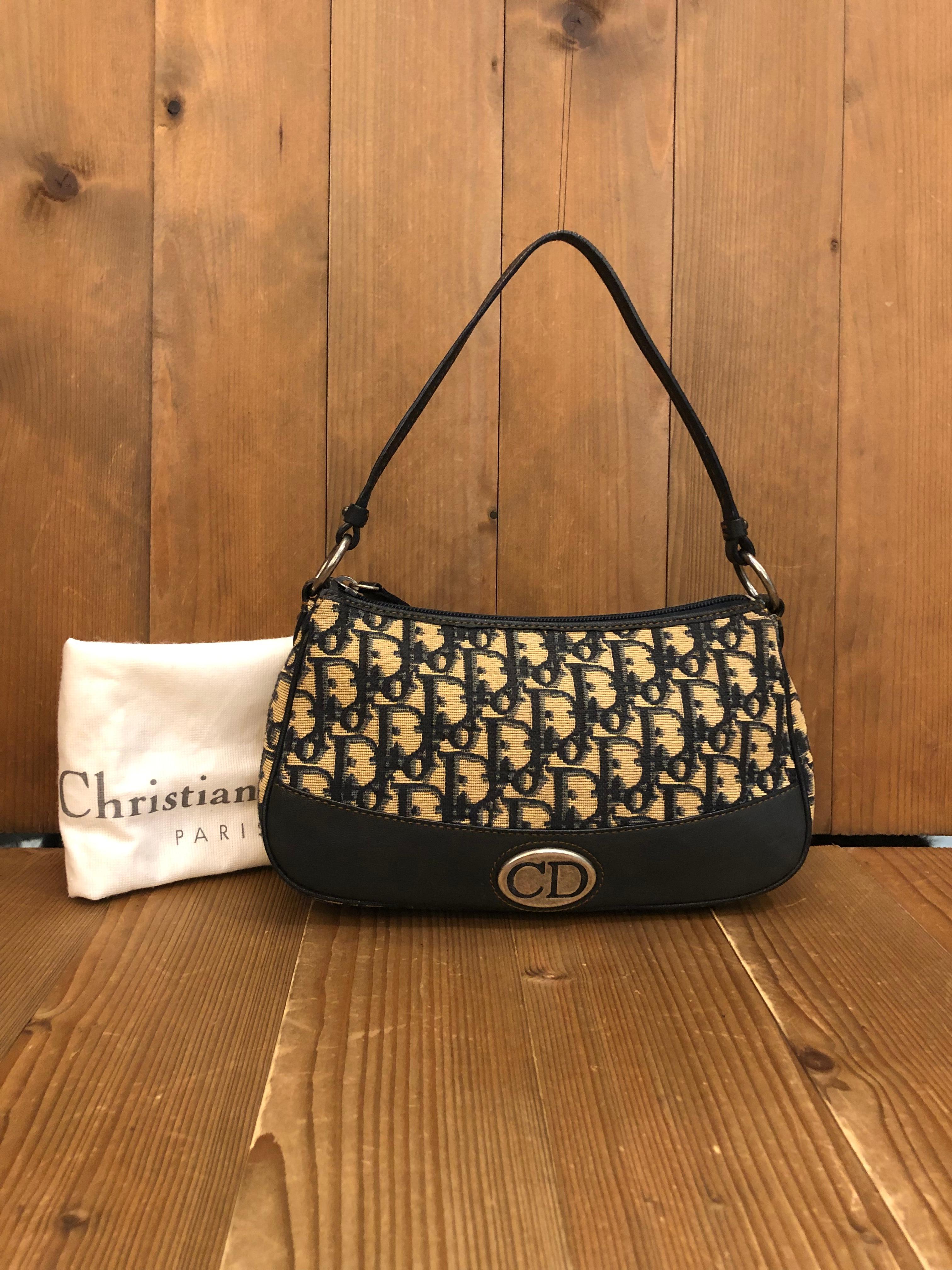 This Christian Dior pouch handbag is crafted of Dior’s iconic trotter jacquard and leather in navy featuring a leather handle that allows you to use it as shoulder pouch. Top zipper closure opens to a navy fabric interior featuring one open pocket.