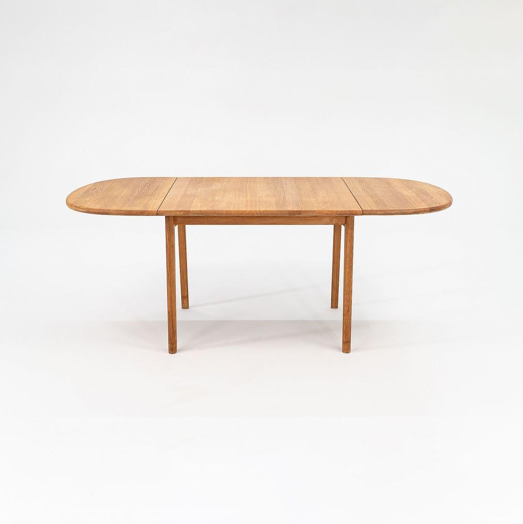 Se trata de una Mesa de comedor CH002, diseñada por Hans Wegner para Carl Hansen & Son en 1960. Este ejemplo data de 2006 y está hecho de roble blanco. La pieza cuenta con hojas extensibles abatibles en cada extremo que se pliegan fácilmente hacia