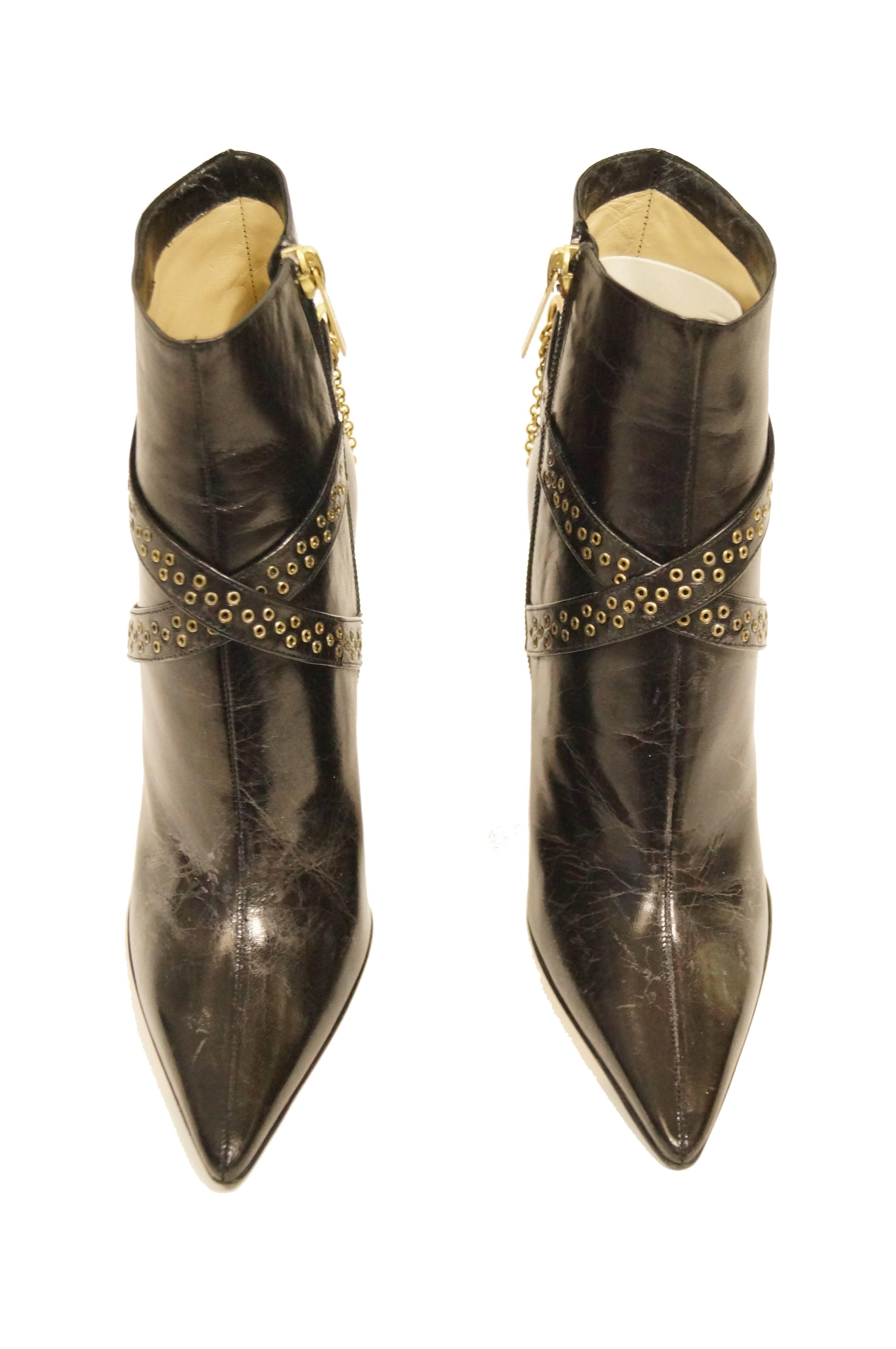 Polished and Edgy smooth point toe booties by Jimmy Choo. The boots feature a thin 4 inch black leather heel with polka dot rivets throughout. Ankles are adorned with crisscross riveted straps with double layered swinging gold chains. Wide boot