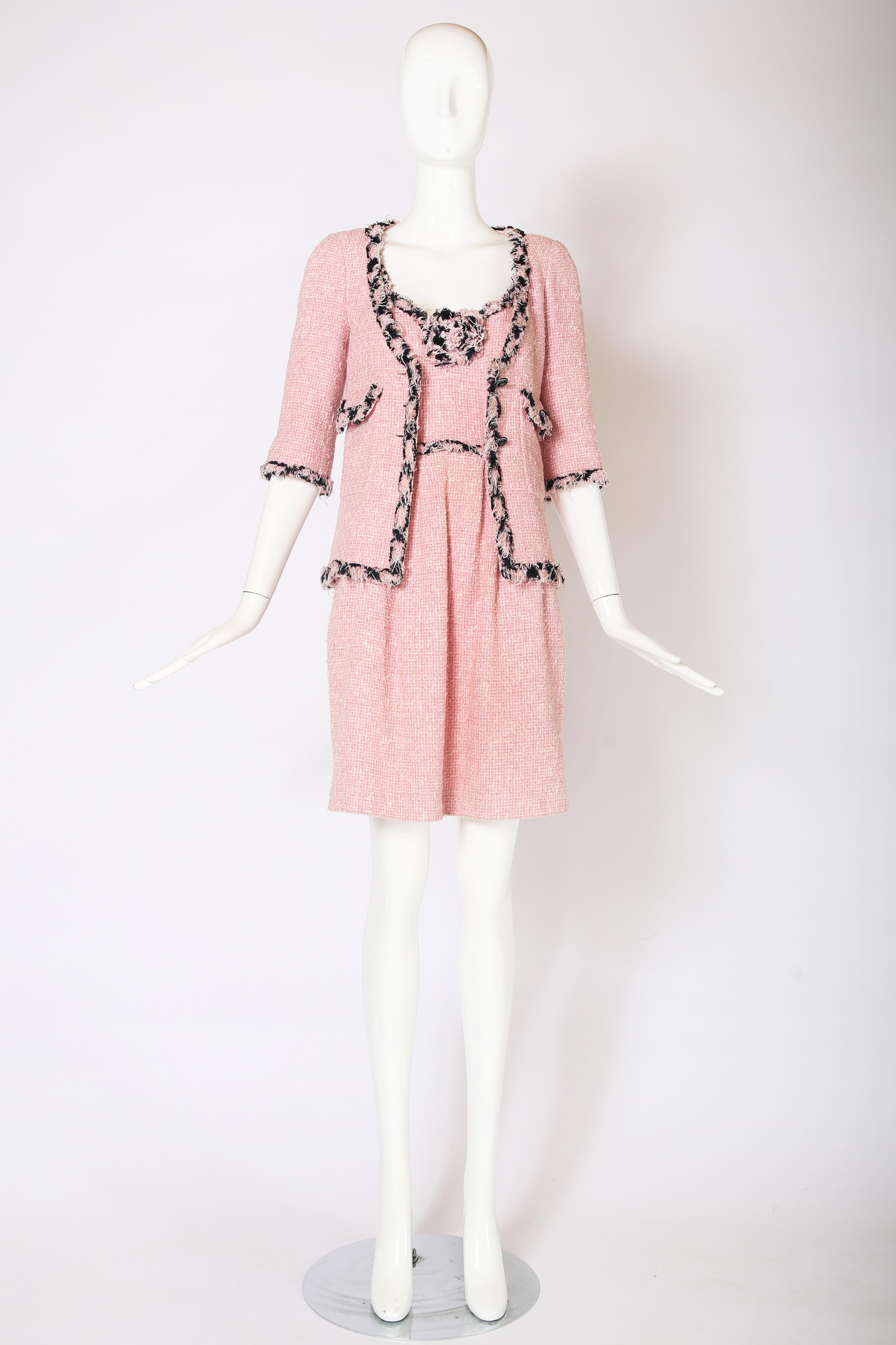 2007 P/E Chanel pink boucle mini dress and jacket ensemble featuring black trim, decorative camellia at front of dress bodice, elbow-length jacket sleeves and silk camellia print at interior lining. Both are Size 34 and in excellent condition. Made