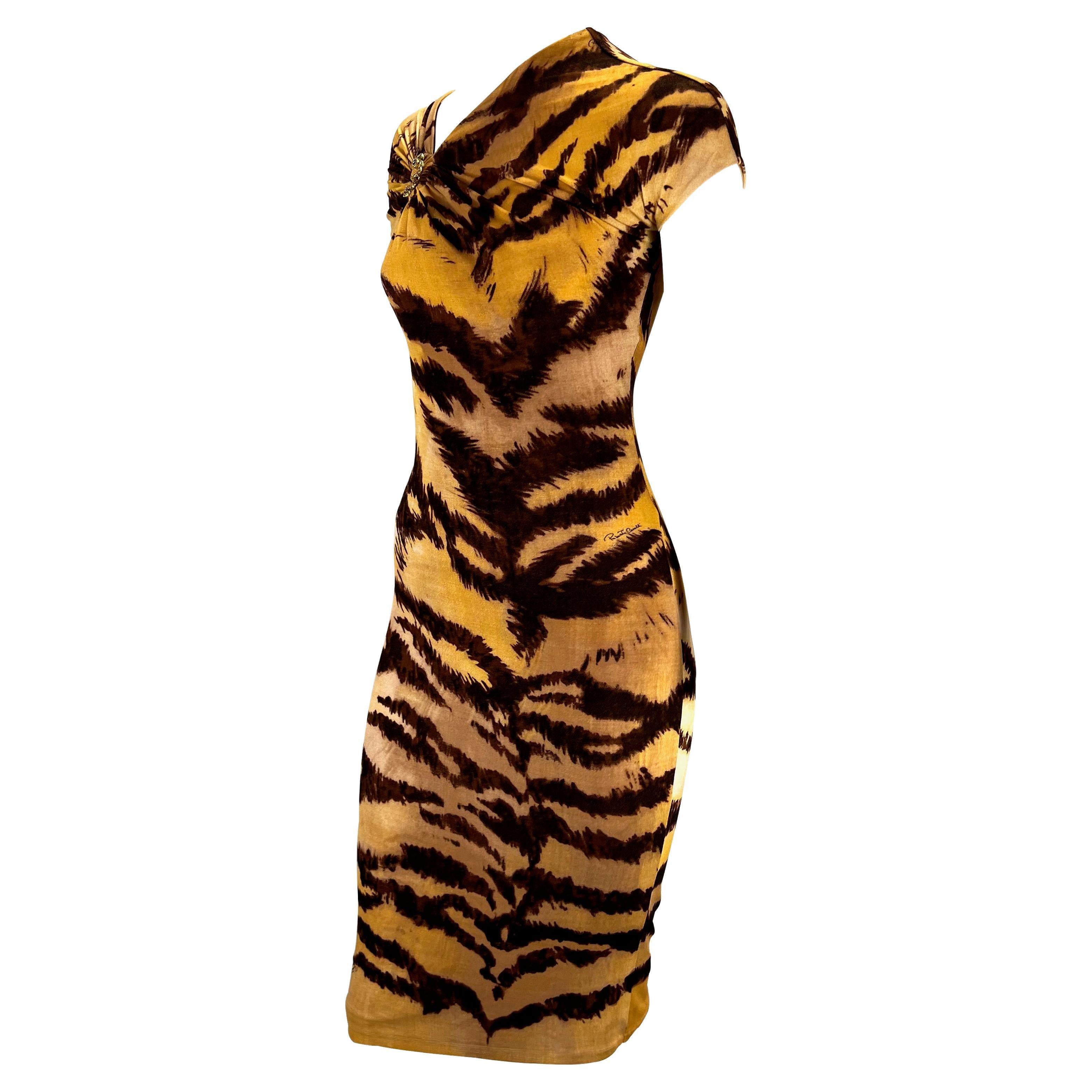 TheRealList presents: a form-fitting tiger print Roberto Cavalli dress. From 2007, this stretchy viscose dress boldly displays a larger tiger print. The dress features an asymetric neckline, petal sleeves, and a gold serpent brooch. Cavalli a master