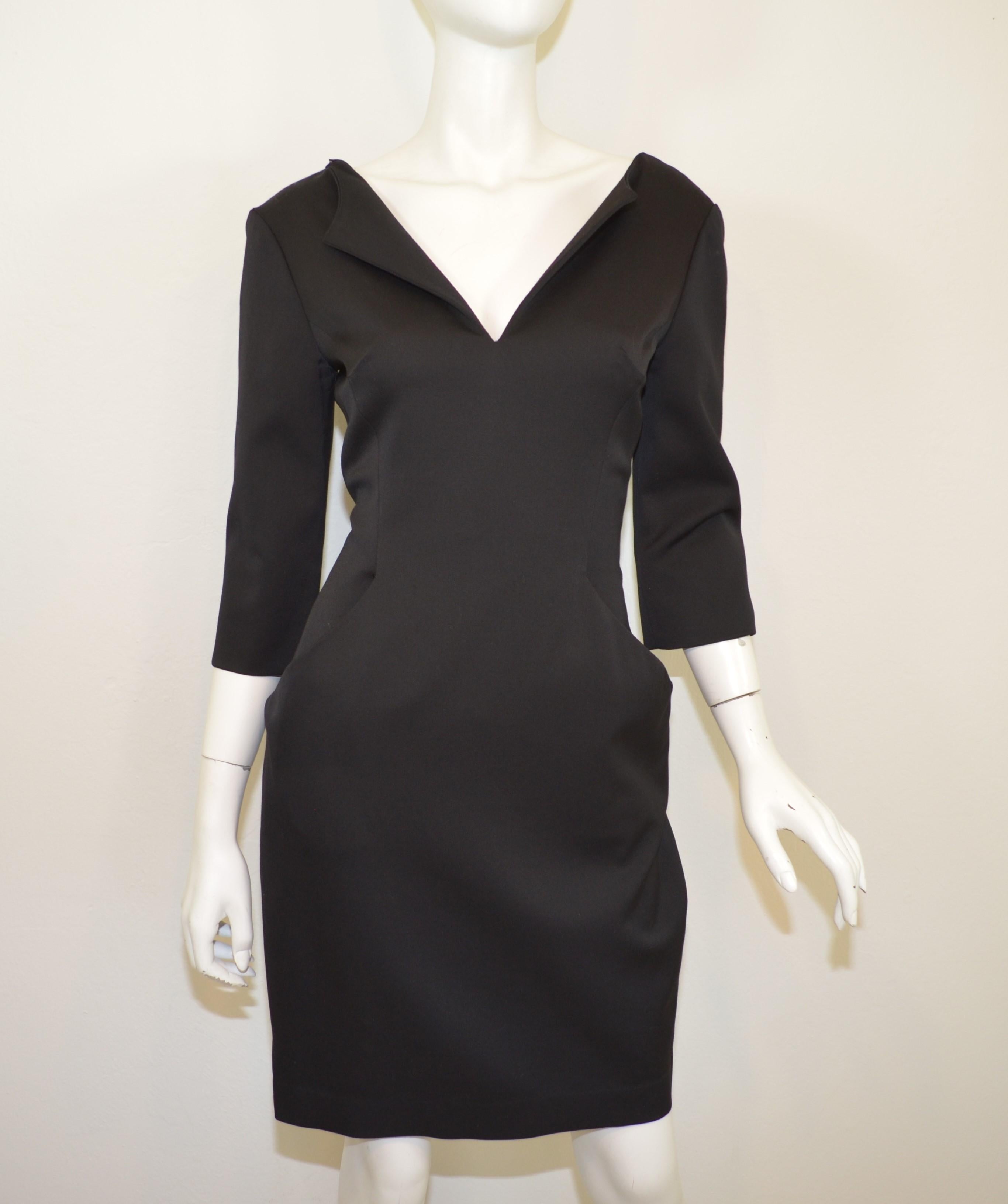 Alexander McQueen black dress is composed in a wool and elastase blend with a fold over v-neckline, 3/4 length sleeves, back zipper and hook-and-eye fastening, and functional pockets at the hips. Dress is labeled size 42, made in