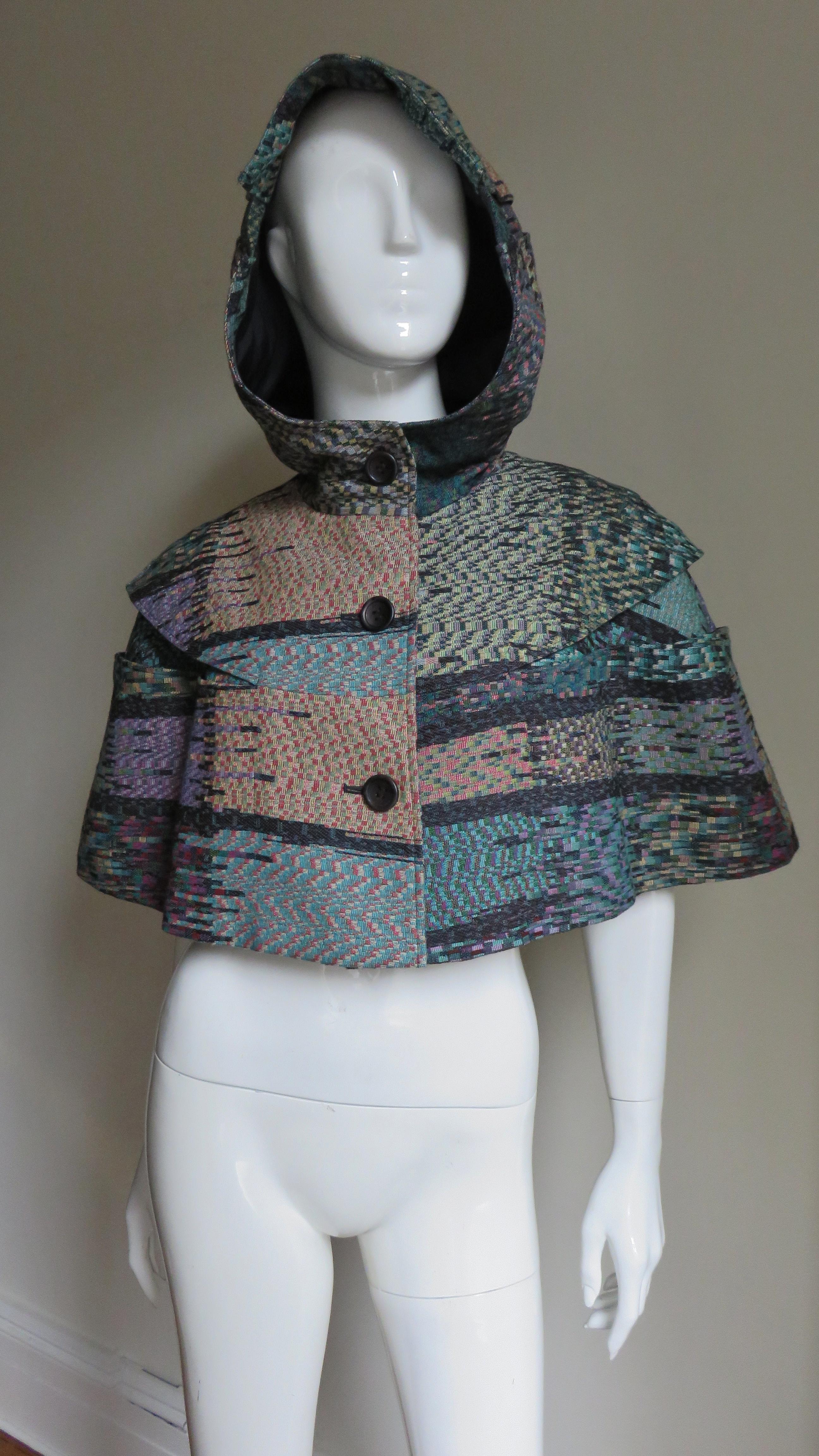 A fabulous wool and silk blend cape from Issey Miyake in green, purple, black and burgundy.  It has a yoke, hood, black buttons up the front and is lined in black.
One size fits most.

Yoke Width  20