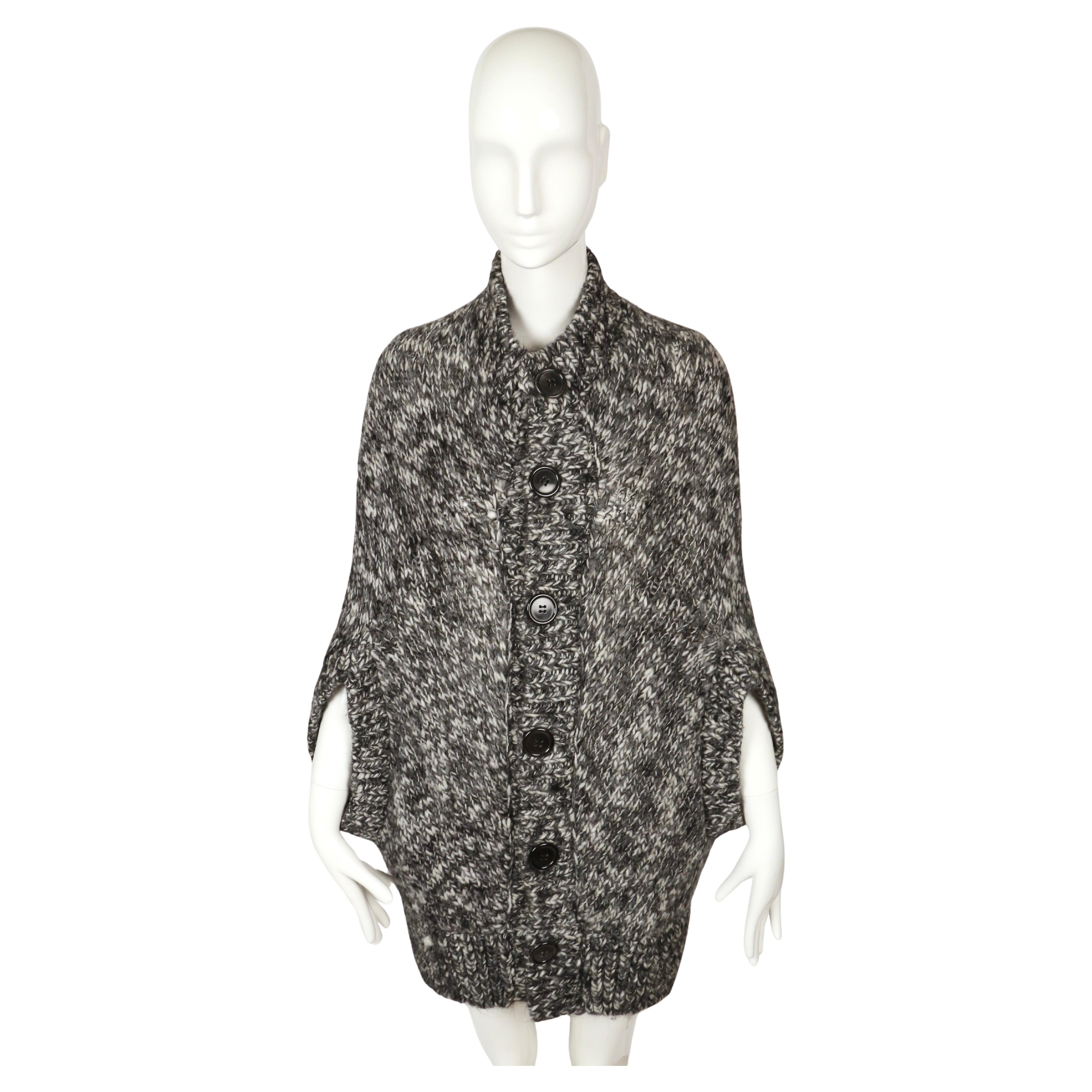 2008 Junya Watanabe Comme des Garçons Strickumhang/Poncho

Das Kleidungsstück ist aus einem dicken, marmorierten Wollstrick in Schwarz- und Grautönen gefertigt, der ihm ein strukturiertes, meliertes Aussehen verleiht. Es ist in einer kokonartigen