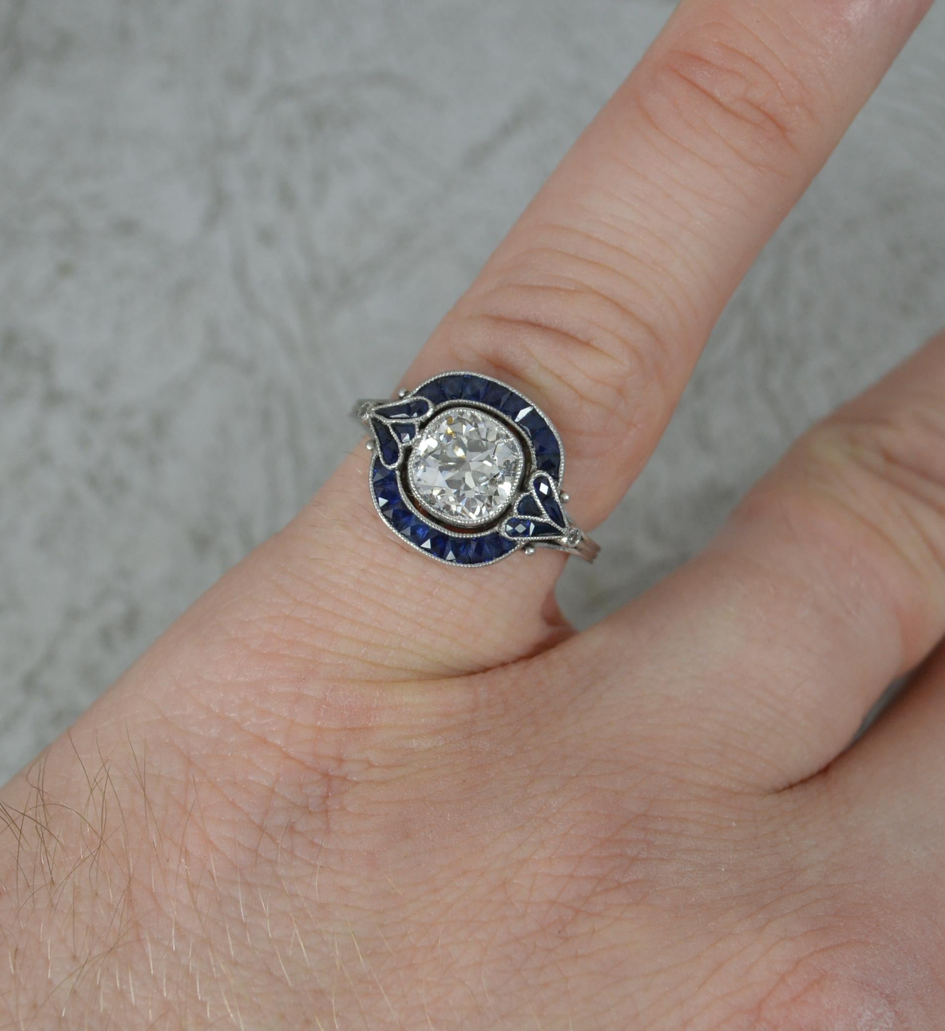 A superb diamond and sapphire target halo engagement ring.
Solid 950 grade platinum shank.
Designed with a 2.00 old mine cut diamond to centre in full grain, bezel setting. I1 clarity, J colour. Bright and sparky. Surrounding are varying size and of