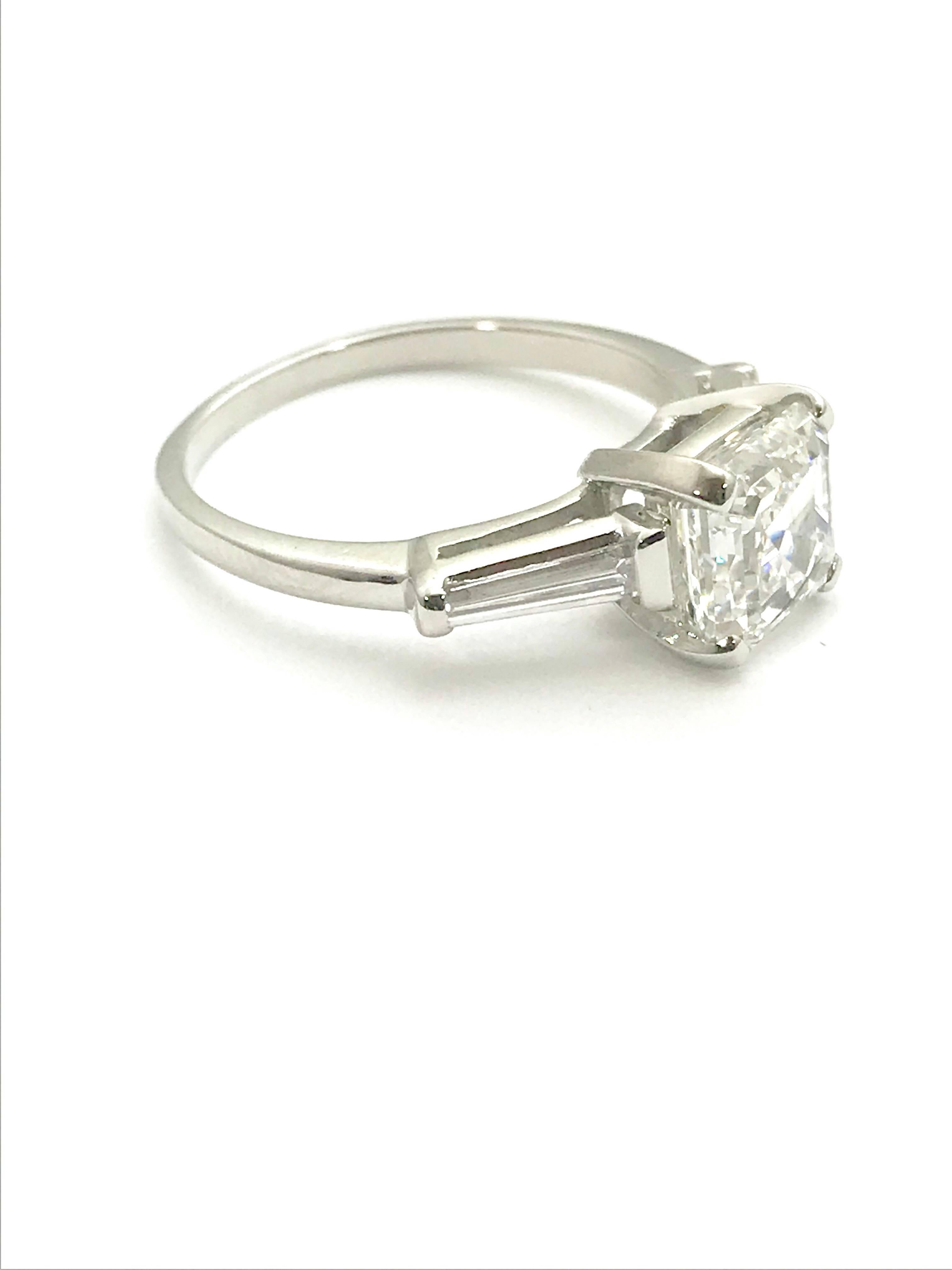 A 2.01 carat asscher cut diamond and tapered baguette platinum engagement ring.  The asscher cut diamond is graded by GIA as a D color, VS2 clarity.  Grading report number 2105632013.  The asscher is set in a four prong basket with two tapered