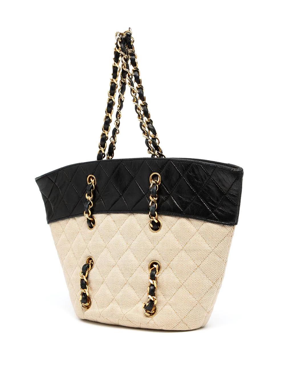 This effortlessly cool Chanel basket-style handbag from 2010-2011 features a diamond-stitched canvas body in a classic beige and a contrasting black lambskin leather top, complemented by the signature Chanel gold-tone chain handles running through