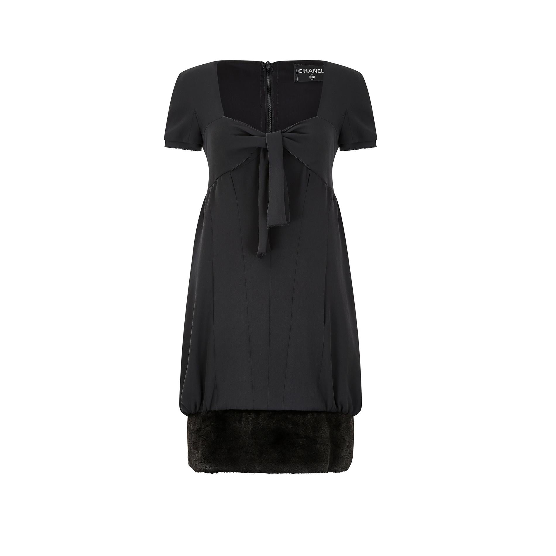 Runway documented Karl Lagerfeld for Chanel, Fall 2010 collection black silk dress with faux fur hem. It features a sweetheart neckline with a front tie bow detail to the chest for a feminine touch. The sleeves are short and finished with a raw hem;