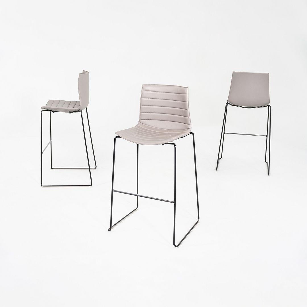 This is a Catifa 46 Bar Stool, originally Designed by Lievore Altherr Molina for Arper in 2004. These particular examples were produced in Italy in the 2010s. The stools feature a clean, minimalist shell upholstered in beige vinyl, paired with a