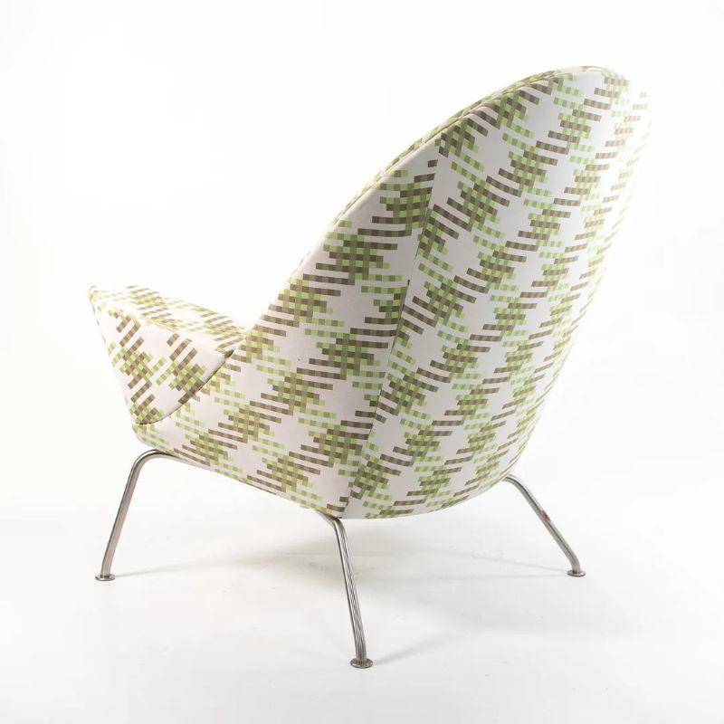Listed for sale is a Oculus Lounge Chair designed by Hans Wegner, produced by Carl Hansen & Son in Denmark. The chair is made with a stainless steel frame and green patterned fabric. This chair dates to circa 2018 and is guaranteed as authentic. The