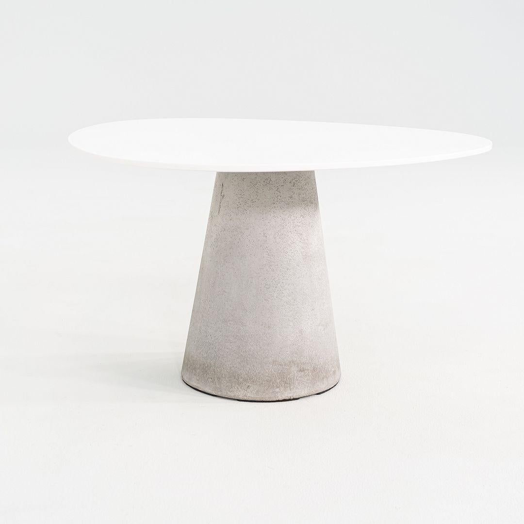 Se trata de una mesa auxiliar Tosca, diseñada originalmente por Wolfgang Mezger para Davis Furniture. Este ejemplo concreto se fabricó en la década de 2010 en Estados Unidos. La mesa presenta una escultural base de hormigón combinada con un tablero