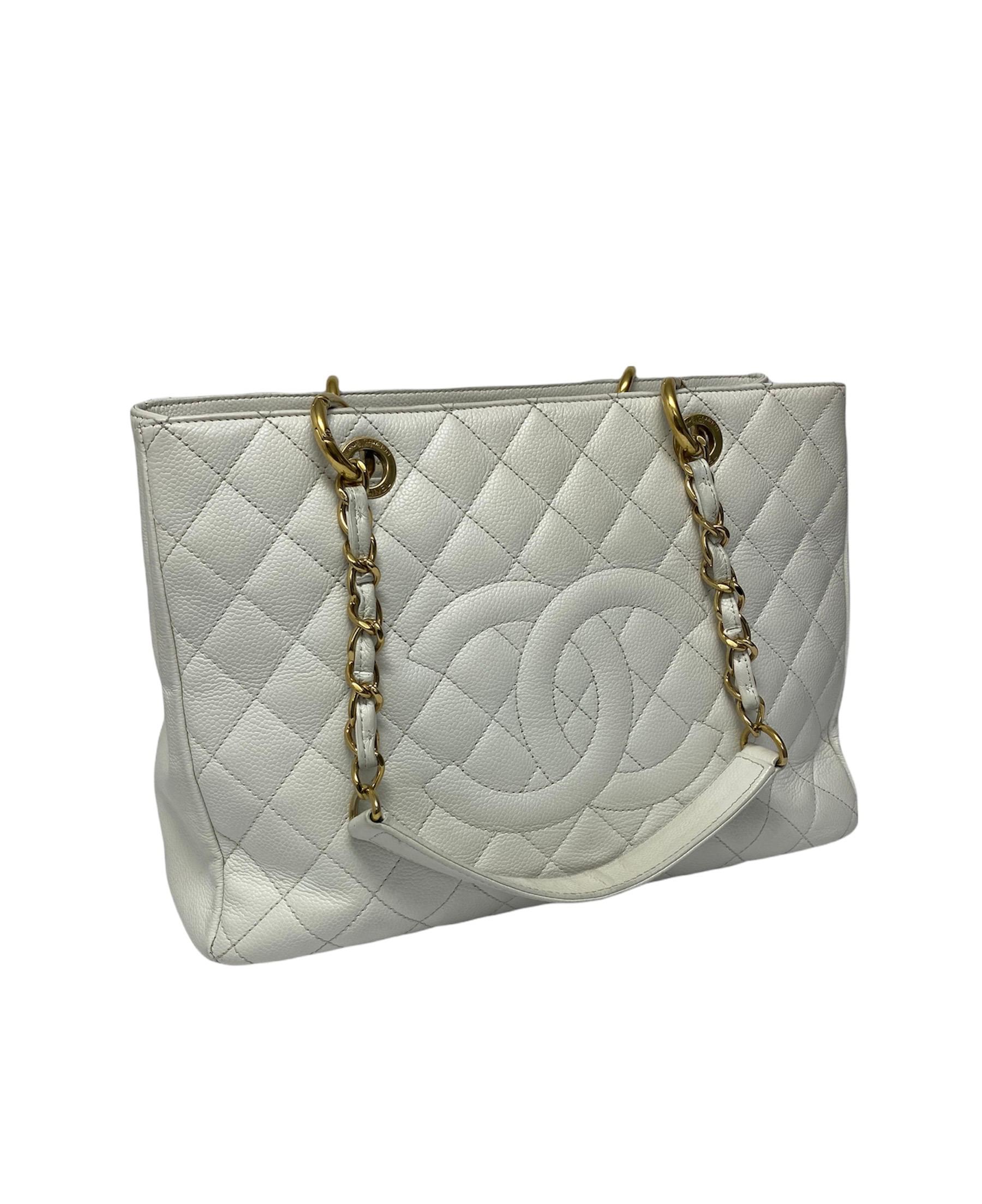 Chanel GST edition bag in white quilted leather with gold hardware.It has a wide central opening and two handles made with a woven chain and black leather. The interiors are lined with a soft gray fabric and inside it is made up of three large