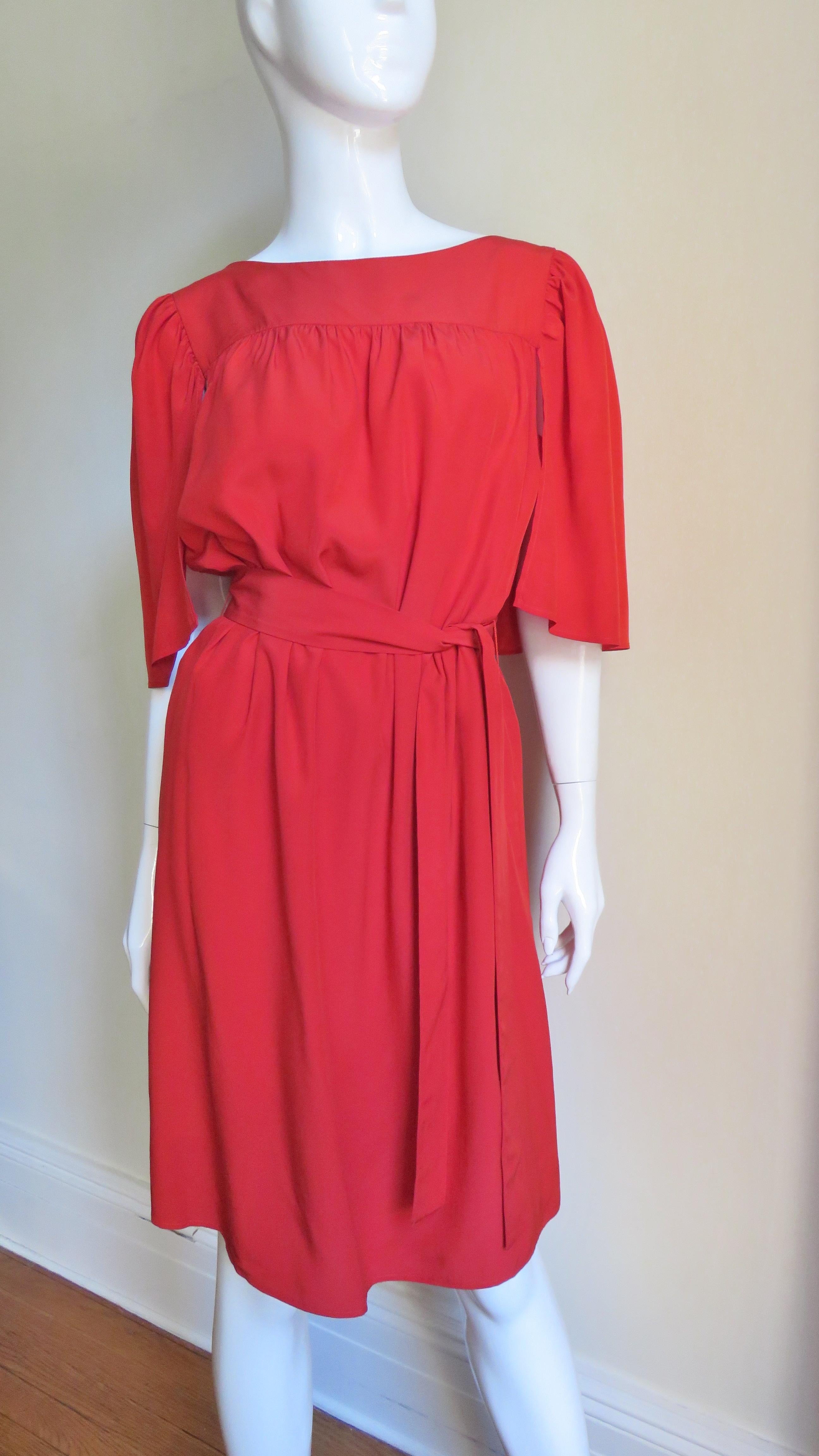 A fabulous red silk dress from Yves St Laurent, YSL 2011 Resort collection.  It has a bateau neckline from which a fabulous caplet falls in the back around to the front shoulders. It comes with a matching tie belt and is lined in matching silk.  No