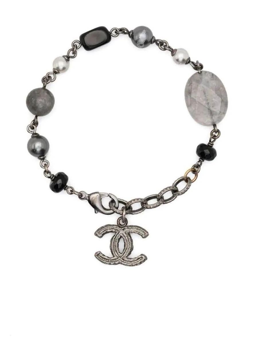Schwarzes Armband von Chanel mit Federringverschluss, einem Logo-Charm, ausgefallenen Perlen und einer entsteinten Plakette. 
Um die 2014er Jahre. 
Länge: 19 cm (7,4 Zoll)
In gutem Vintage-Zustand. Hergestellt in Frankreich. 
Wir garantieren Ihnen,