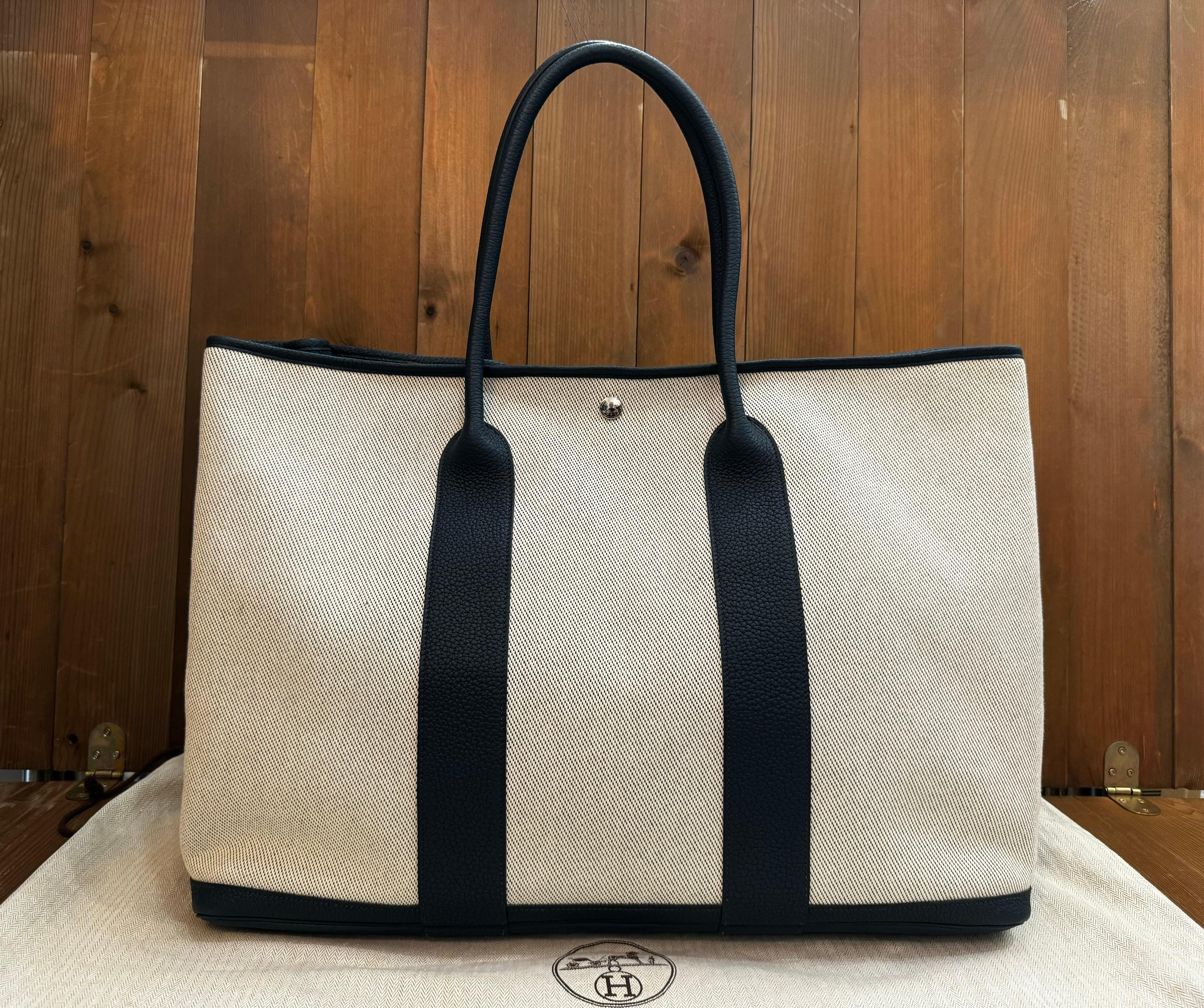 This 2014 HERMES Ecru Toile H Canvas Bleu de Prusse Cuir Negonda Garden Party 49 Voyager tote bag is crafted of off-white canvas and dark blue large-grained calfskin leather. Top wide opening with snap fastening opens to a spacious unlined interior.