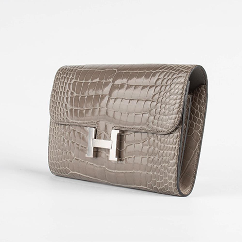 Crafted in France from shiny alligator leather in a highly sought shade of gris tourtarelle, this Hermès Constance Long Wallet showcases a classic flap top design, two wall pockets to the front and a single wall pocket to the rear. The brand's