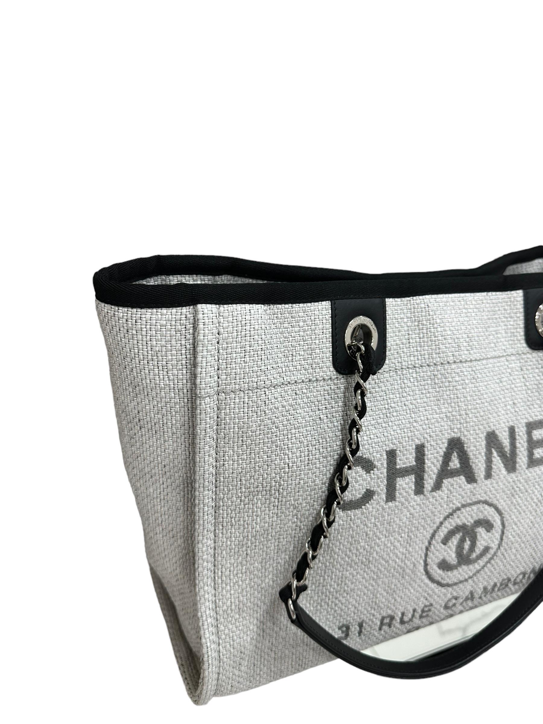 Borsa firmata Chanel, modello Deauville, realizzata in rafia grigio chiaro con inserti in tela nera e hardware argentati. Dotata di una chiusura centrale calamitata, internamente rivestita in tela nera, molto capiente. Munita di doppio manico a