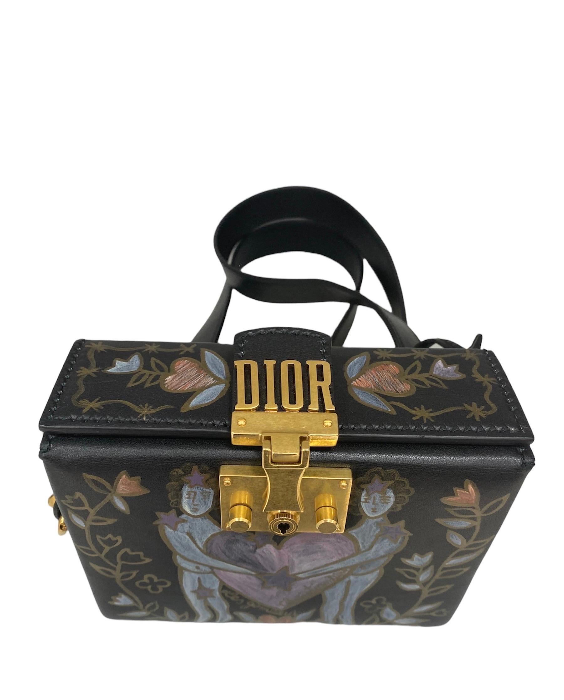 Bag signed Dior model LockBox made of smooth black leather with front painting depicting the symbol of cufflinks and gold hardware.

Equipped with a removable black leather shoulder strap. Equipped with an interlocking closure with writing preceding