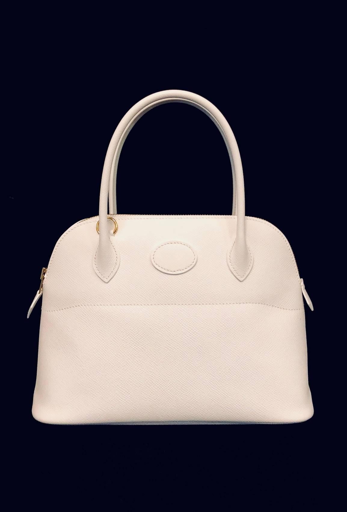 Introduced by Emile-Maurice Hermes in 1923, the Bolide has become a classic and instantly recognizable design! Features gold tone hardware, ultra-luxurious white Epsom leather all over, single zip closure, and an oval patch. Bag easily transforms to