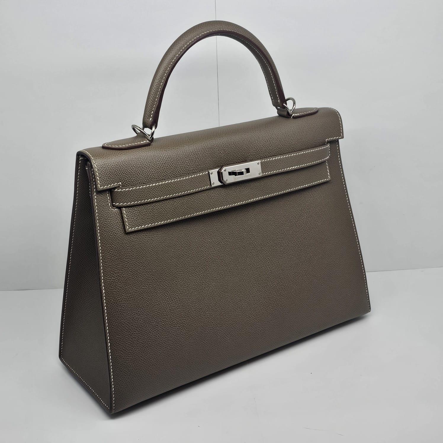 Classique Hermes Kelly 32 Etoupe Epsom avec des ferrures en palladium. Comme un état neuf. Signes d'usure très minimes. Livré avec son sac à poussière, ses outils, son imperméable et sa copie de reçu (prix barré).