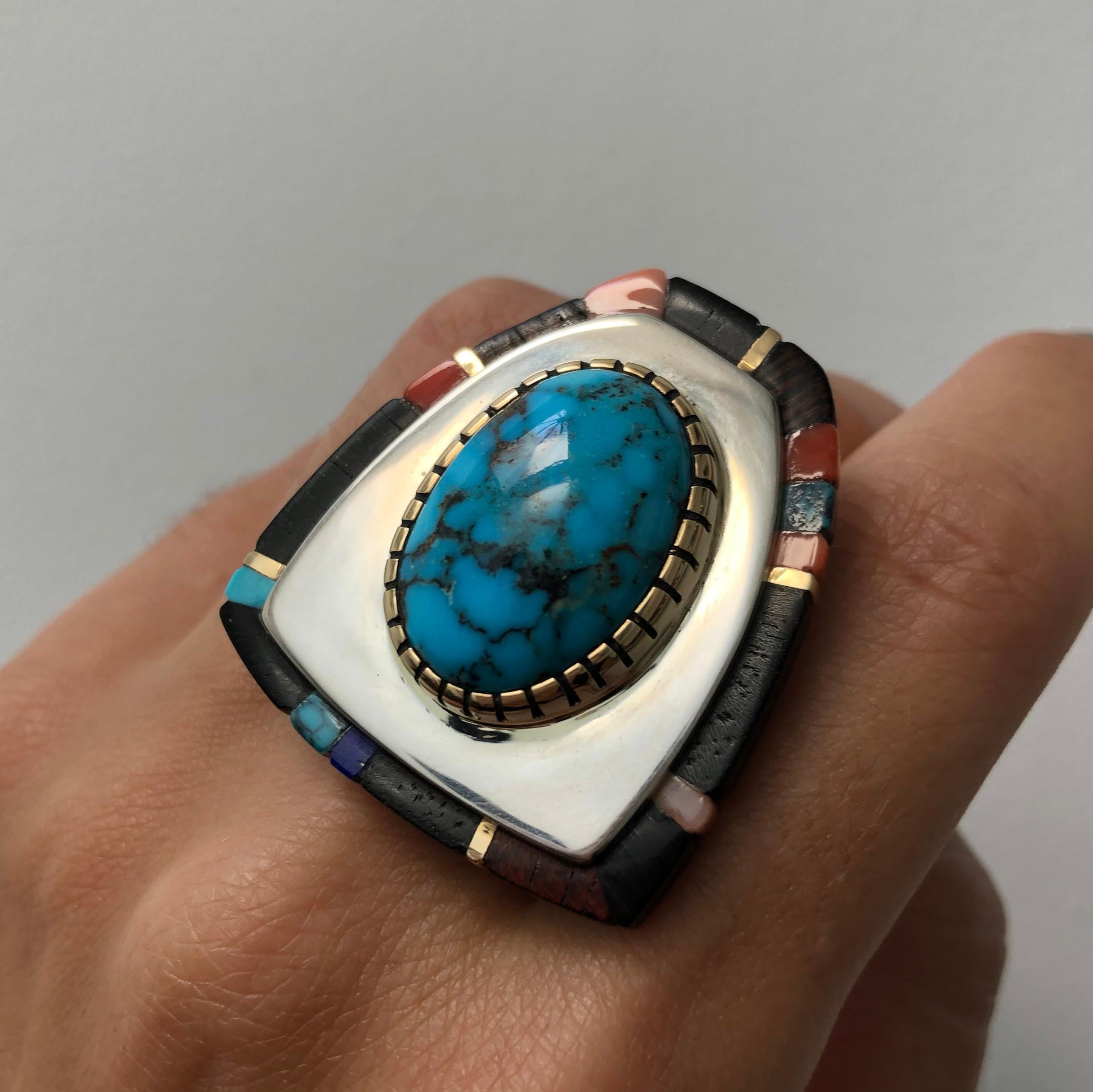 A Candelaria turquoise, lapis, ebony, coral, 18 karat gold and sterling silver ring, by master Hopi goldsmith Sonwai (Verma Nequatewa), 2017.  Signed Sonwai. Ring size 7.25. 

This rare turquoise cabochon comes from the Candelaria mines in