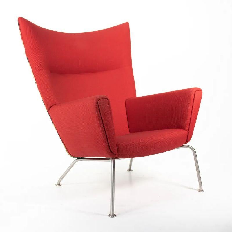 La vente porte sur une (deux chaises sont disponibles, le prix indiqué est pour chaque chaise) CH445 Wing Lounge Chair composée d'une structure en acier inoxydable et d'un tissu rouge avec un motif floral sur le dos. Les chaises ont été conçues par