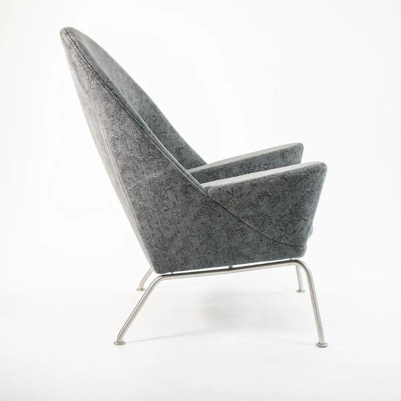 Listed for sale is a Oculus Lounge Chair designed by Hans Wegner, produced by Carl Hansen & Son in Denmark. The chair is made with a stainless steel frame and grey fabric. This chair dates to circa 2018 and is guaranteed as authentic. Condition is