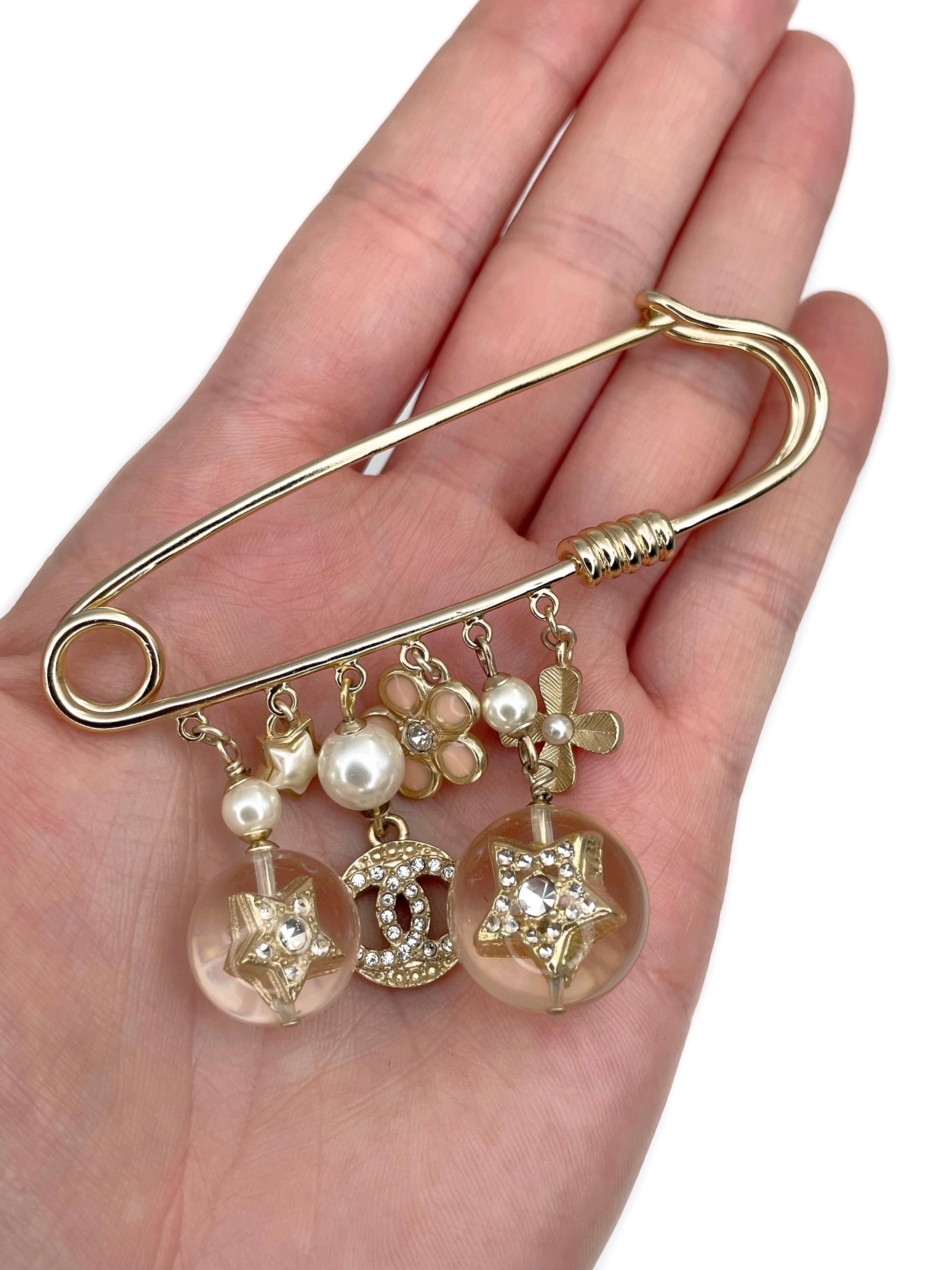This is a charm safety pin brooch designed by Chanel for 2019 collection. The piece is gold plated. It features CC logo, star, flower, clover charms. They are adorned with clear crystals, faux pearls, enamel, lucite. 

Signed: ©Chanel® A19K. Made in