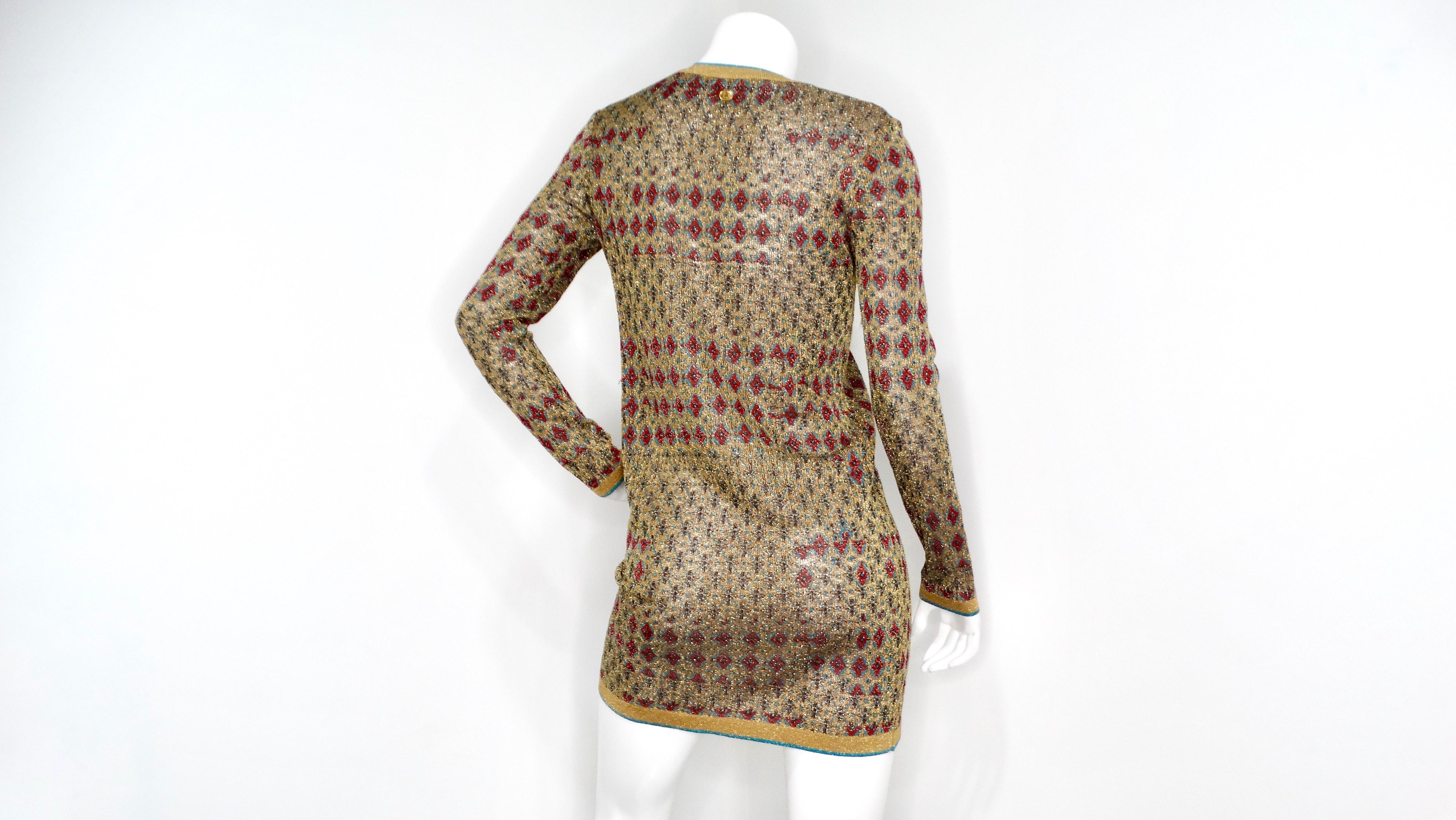 The 2019 Chanel Metallic Gold-Tone Knit Egypt Collection Mini Dress is a striking piece that blends metallic gold knit with vibrant red and turquoise blue accents. This long-sleeve dress features an intricate diamond-shaped knit pattern, providing a