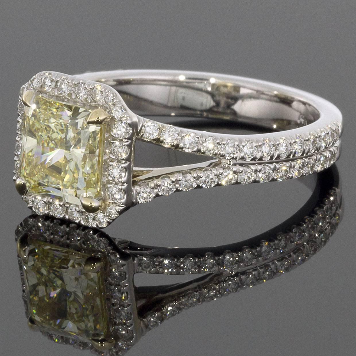 This gorgeous halo engagement ring features a stunning 1.51 carat radiant cut center diamond that grades as Fancy Light Yellow in color & VS1 in clarity. It is surrounded by a cushion shaped halo of brilliant white diamonds that also extend down the