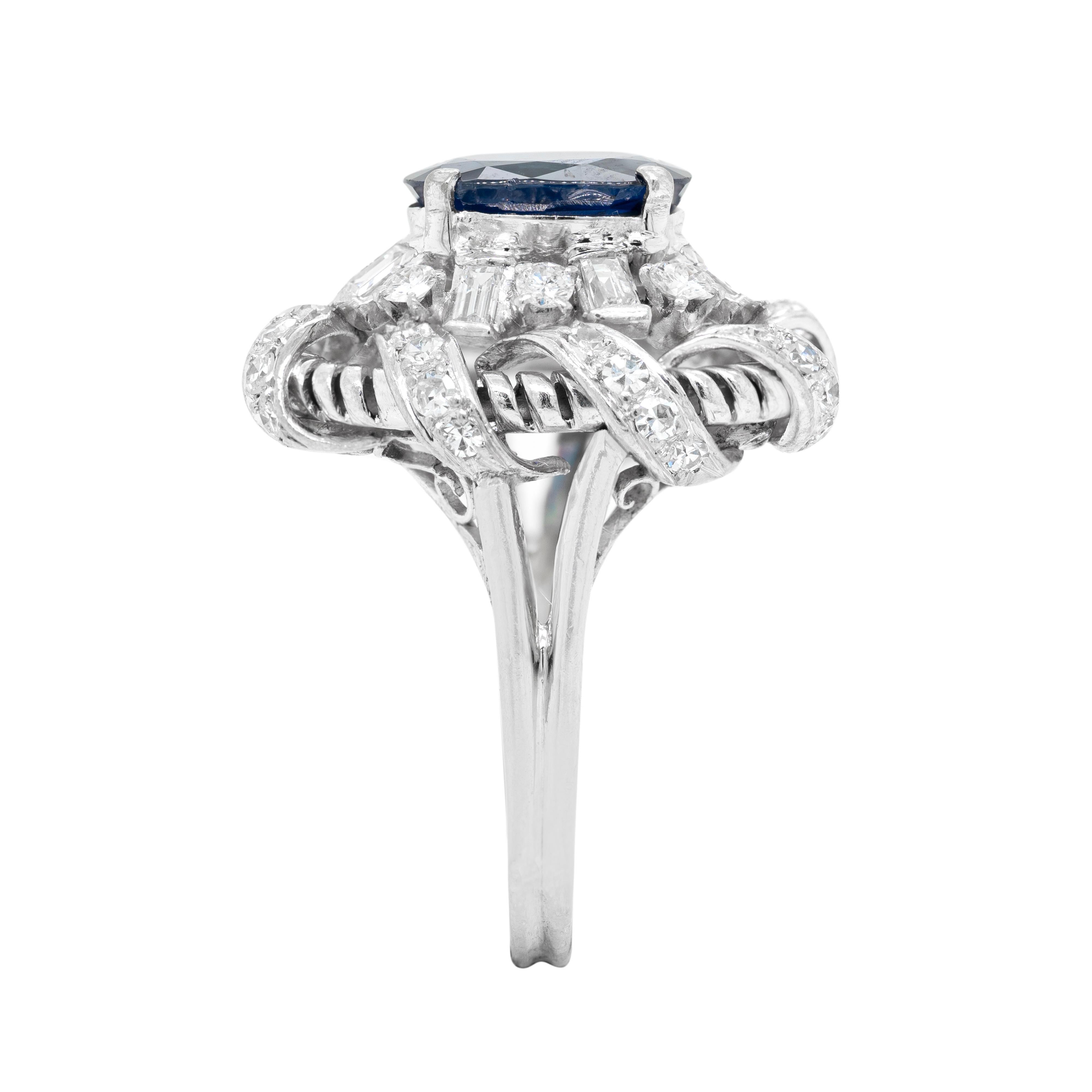 This wonderful vintage platinum cluster ring features a natural unheated  Burmese royal blue oval sapphire weighing 2.02ct in a four claw, open back setting. The vibrant stone is beautifully surrounded by a row of alternating semi rub-over set