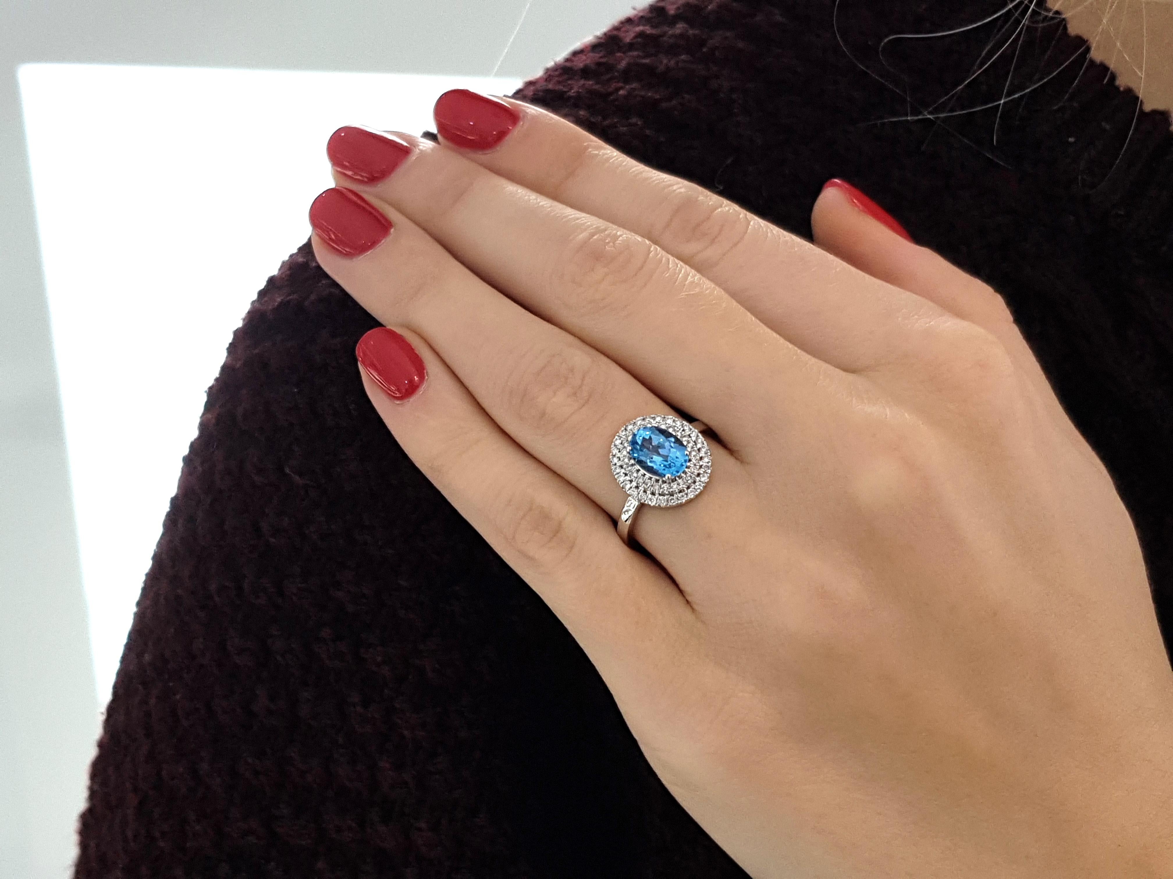 This beautiful 1.70 Carat oval cut Blue Topaz engagement ring surrounded by double halo 0.32 Carat Round White Brilliant Cut Diamonds color H clarity SI1 set in 18 Karat white gold. The ring has a total gem weight of 2.02 Carat. UK size M, US size 6