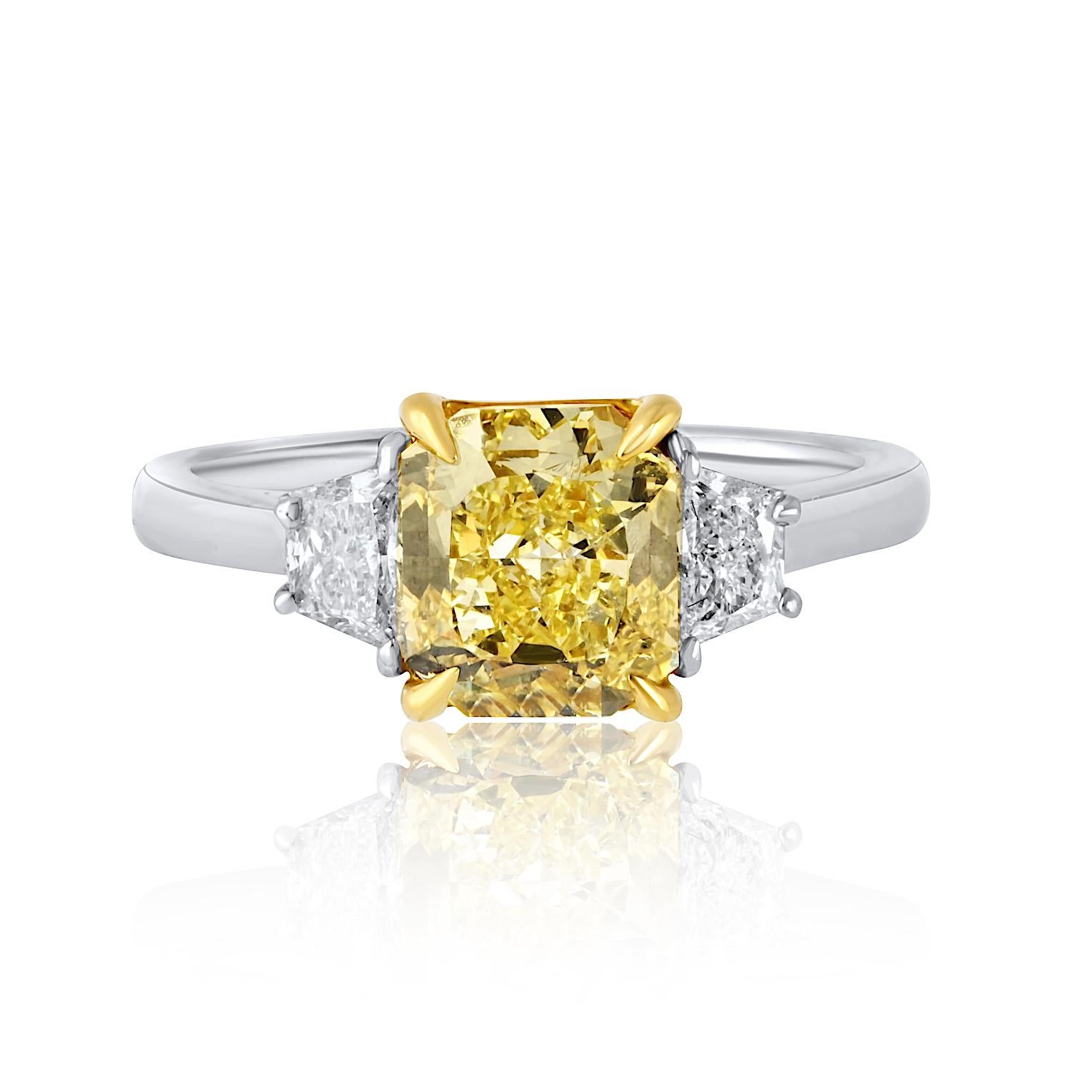 This exquisite handmade engagement ring showcases a breathtaking 2.02-carat radiant cut diamond with a vivid Fancy Intense Yellow hue, GIA certified for its exceptional color and VS clarity. Flanking the center stone are two brilliant trapezoid cut