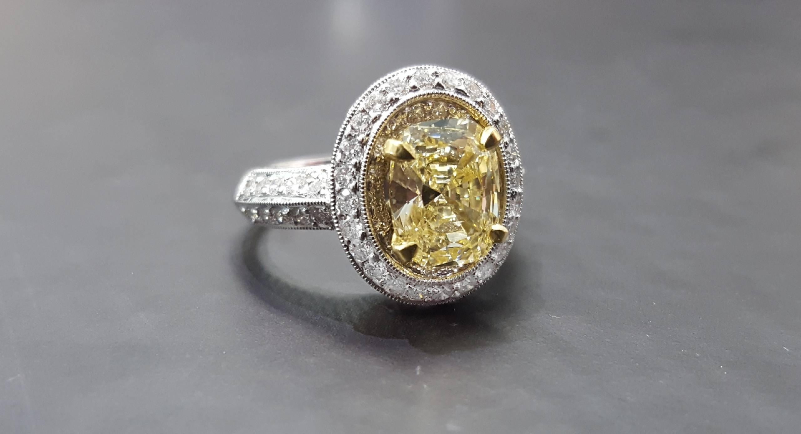 An 18 karat white gold ring set with a 2.02 Fancy Light Yellow Cushion cut diamond. The center diamond is Si2 clarity. The mounting is set with 62 Round Brilliant cut diamonds that weigh approximately 1.00cttw. The ring is a size 7. 