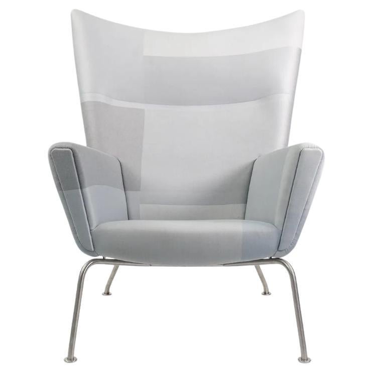 Listed for sale is a CH445 Wing Lounge Chair and Ottoman, made with a stainless steel frame and grey color blocked fabric. The set was designed by Hans Wegner and produced by Carl Hansen & Son in Denmark. The set dates to circa 2020 and is