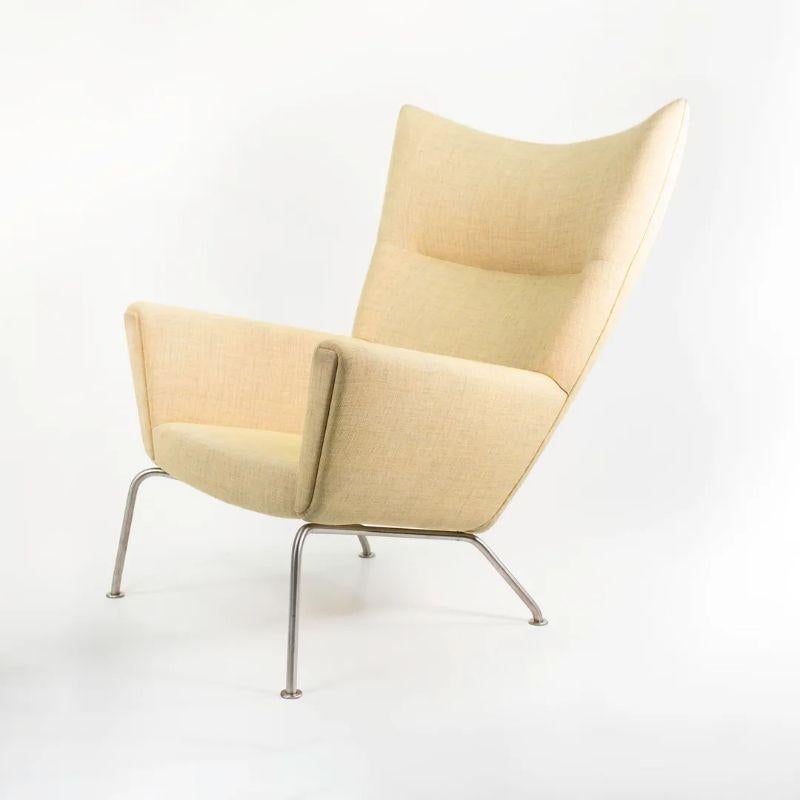 Zum Verkauf steht ein CH445 Wing Lounge Chair mit einem Gestell aus Edelstahl und hellgelbem Stoff. Der Stuhl wurde von Hans Wegner entworfen und von Carl Hansen & Son in Dänemark hergestellt. Der Stuhl stammt aus der Zeit um 2020 und ist garantiert