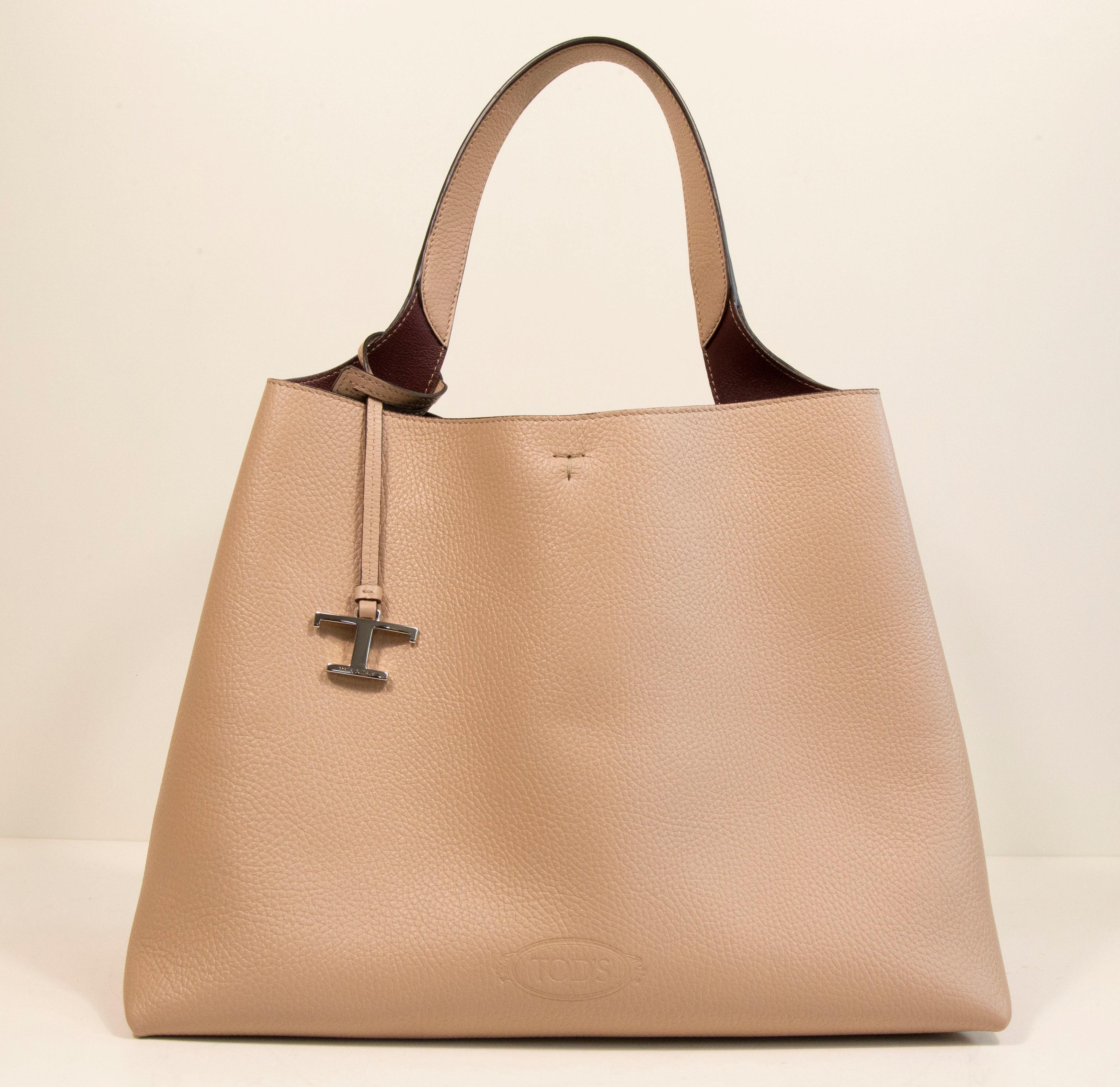 A medium TOD's shoulder bag made of hammered leather in nude/beige leather with silver toned hardware. The interior is lined with smooth bordeaux leather, and it consists of two compartments separated by a zipped leather pouch. The bag features