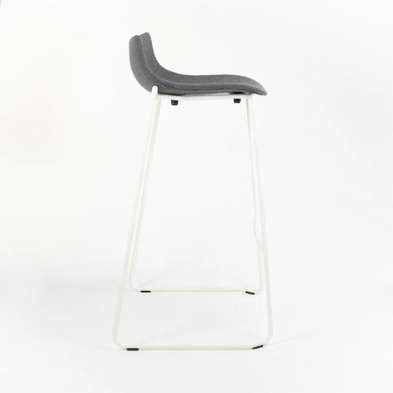This is a BA004F Preludia Bar Stool, designed by Brad Ascalon and produced by Carl Hansen & Son in Denmark. The stool is made with a white powder-coated steel frame and a gray Fjord 17 fabric seat. The stool dates circa 2021 and is guaranteed as