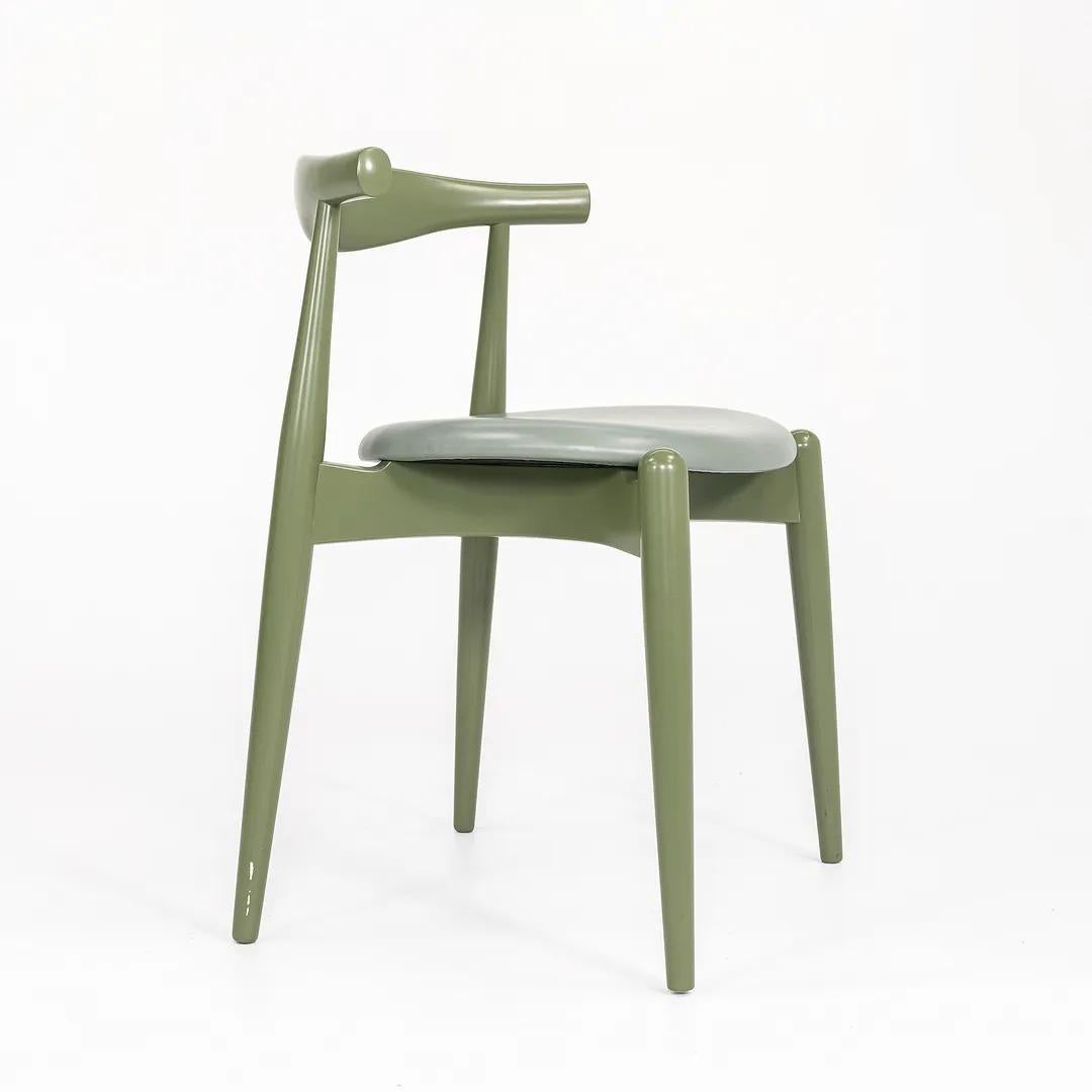 This is a CH20 Elbow Dining Chair made with a solid beech frame, painted green, and an olive leather seat. The chair, designed by Hans Wegner and produced by Carl Hansen & Son in Denmark, dates to circa 2021 and is guaranteed as authentic. Condition