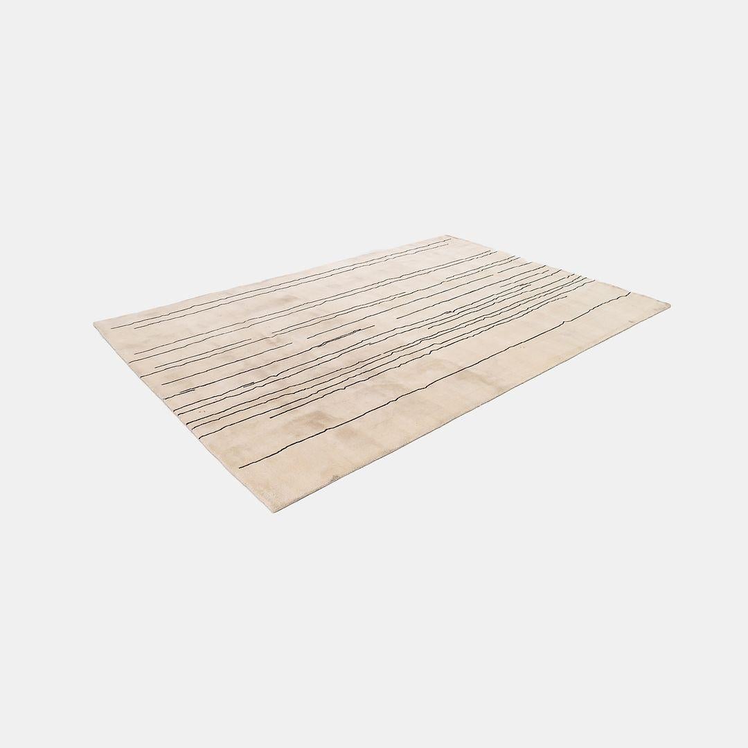 Il s'agit d'un tapis Woodlines, conçu par Naja Utzom Popov et produit par Carl Hansen au Danemark. La pièce est réalisée en fil de laine noué à la main, de couleur crème, et présente des lignes noires contrastantes. Le tapis date d'environ 2021 et