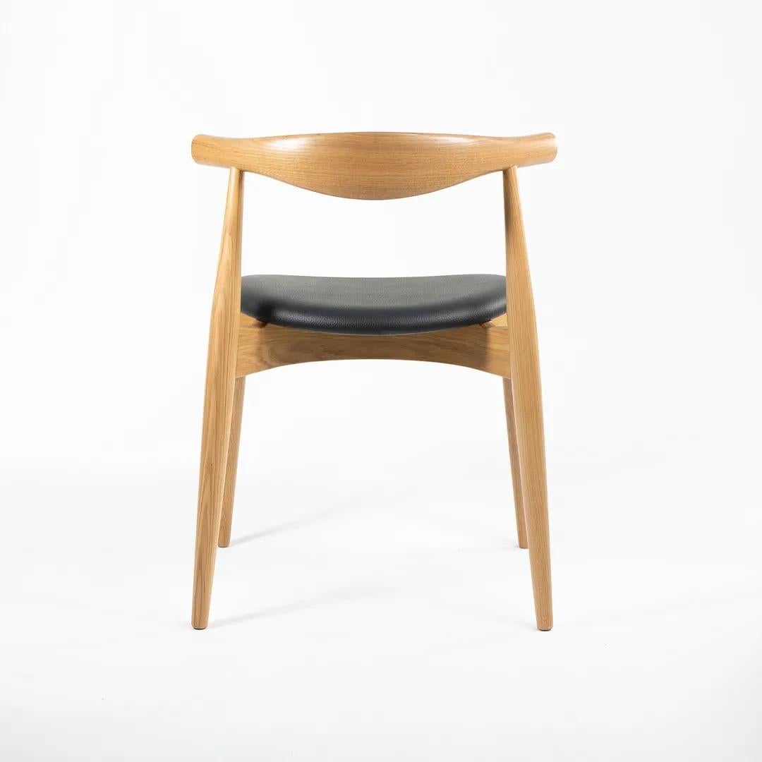 Il s'agit d'une chaise de salle à manger CH20 Elbow, composée d'un cadre en chêne massif laqué et d'une assise en cuir noir. La chaise, conçue par Hans Wegner et produite par Carl Hansen & Son au Danemark, date d'environ 2021 et est garantie