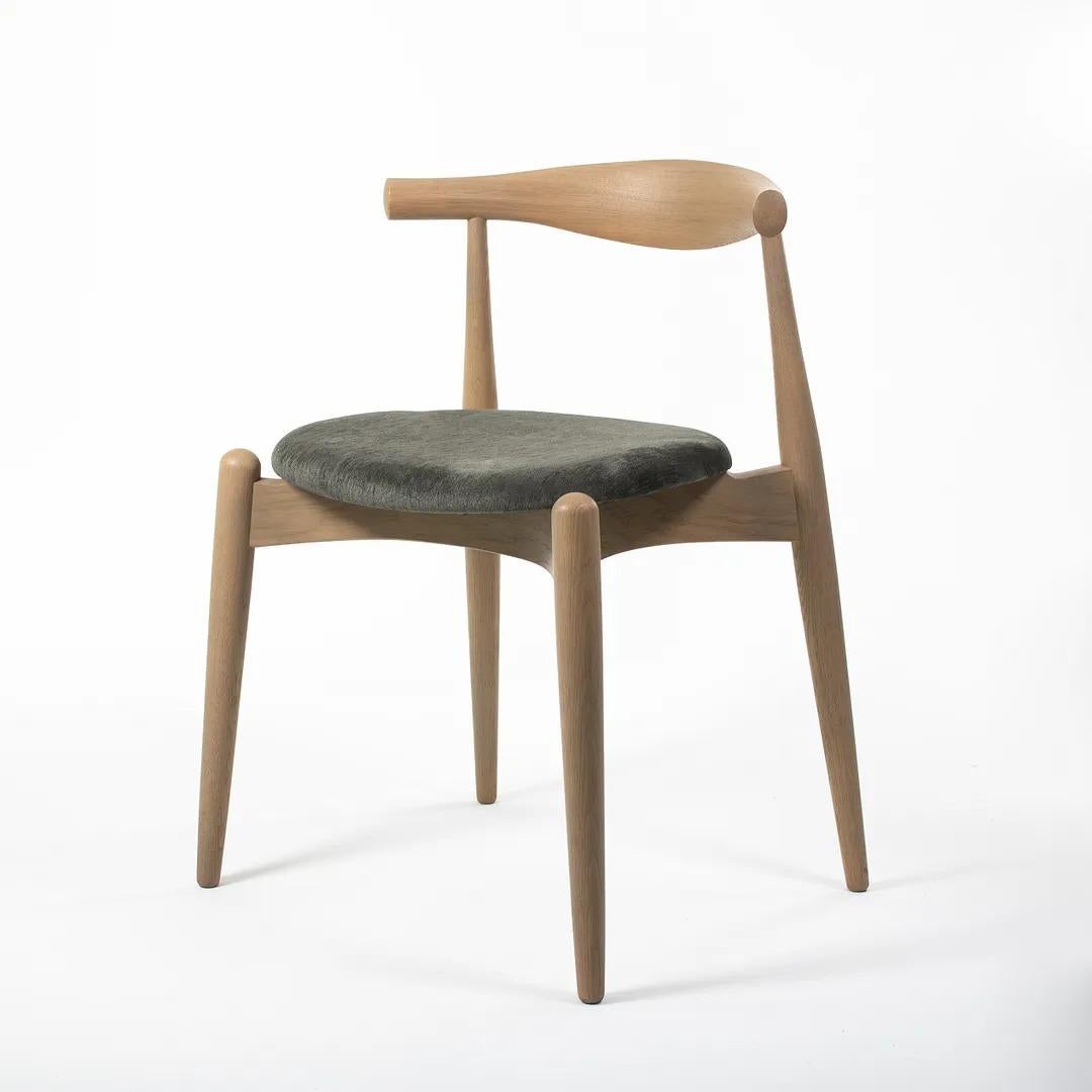 Il s'agit d'une chaise de salle à manger coudée CH20 fabriquée avec une structure en chêne massif savonné et une assise en tissu gris/vert. La chaise, conçue par Hans Wegner et produite par Carl Hansen & Son au Danemark, date d'environ 2021 et est