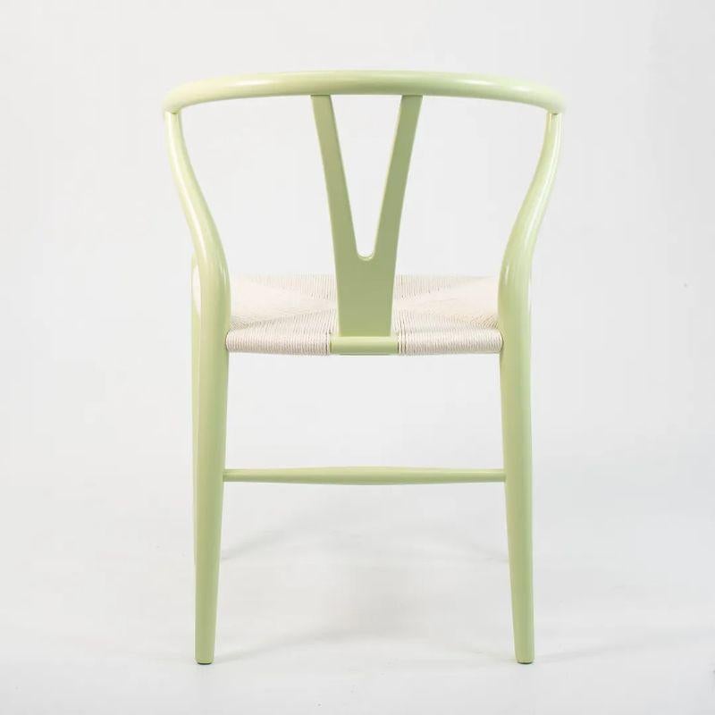 Il s'agit d'une chaise de salle à manger CH24 Wishbone, conçue par Hans Wegner et produite par Carl Hansen & Son au Danemark. La chaise est composée d'une structure en hêtre massif, peinte en vert menthe avec une assise en cordon de papier blanc.