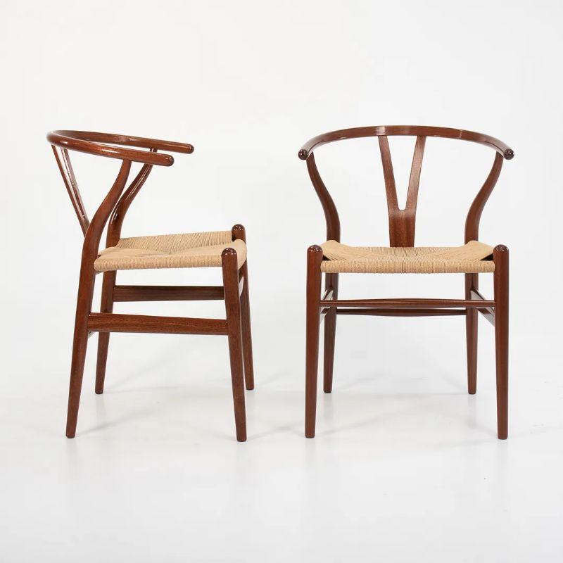 These are three (sold separately) Wishbone dining chairs, designed by Hans Wegner and produced by Carl Hansen & Son in Denmark. The chairs are made with a solid glossy lacquered mahogany frame with a natural paper cord seat. These chairs date to