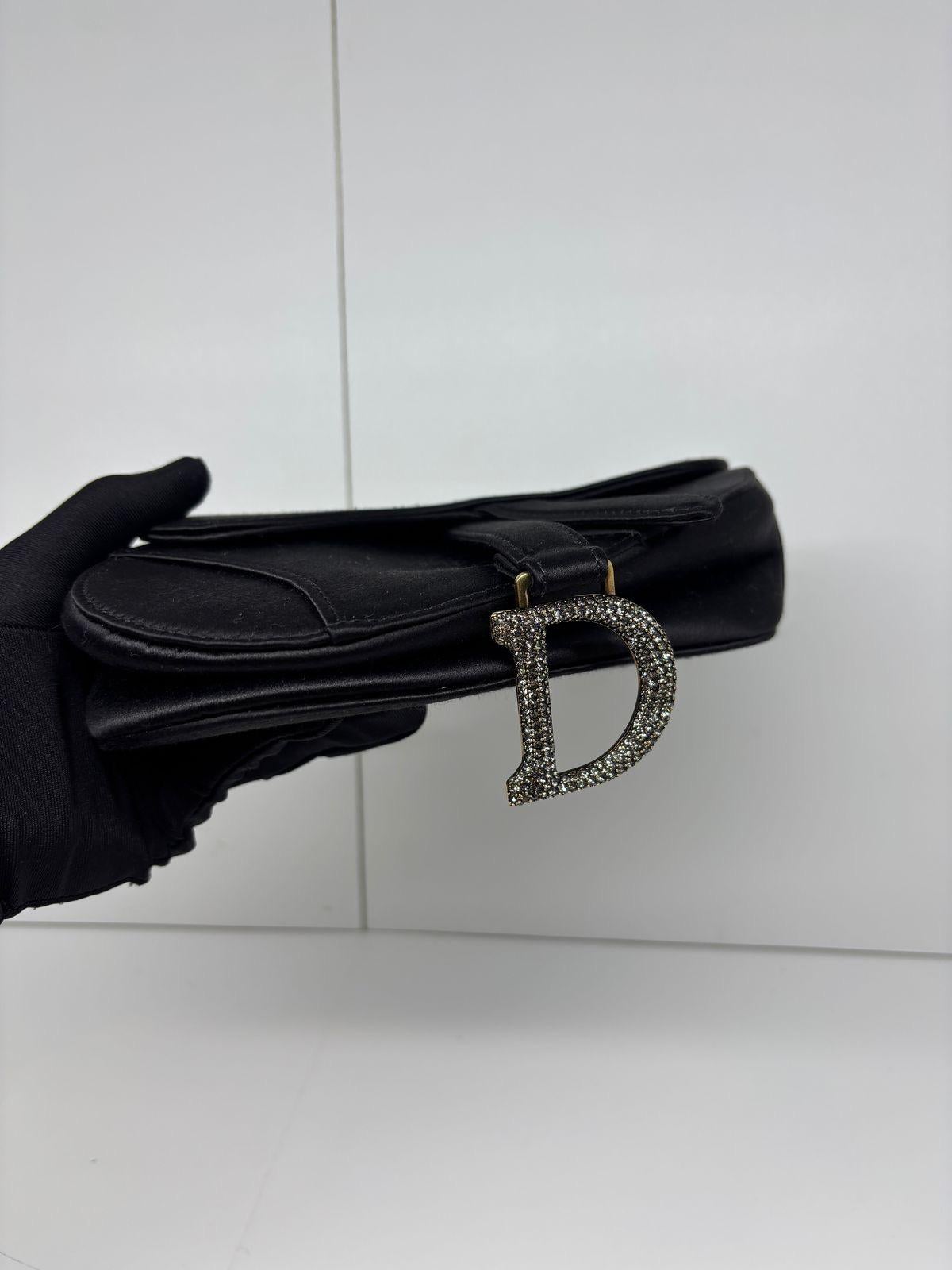 Beautiful mini saddle bag in elegant black satin with gold hardware encrusted with Swarovski crystal. Minor rubbing on the satin logo label inside. Date stamp from 2021. No snagging on the satin surface. Very beautiful coveted piece. Comes only with