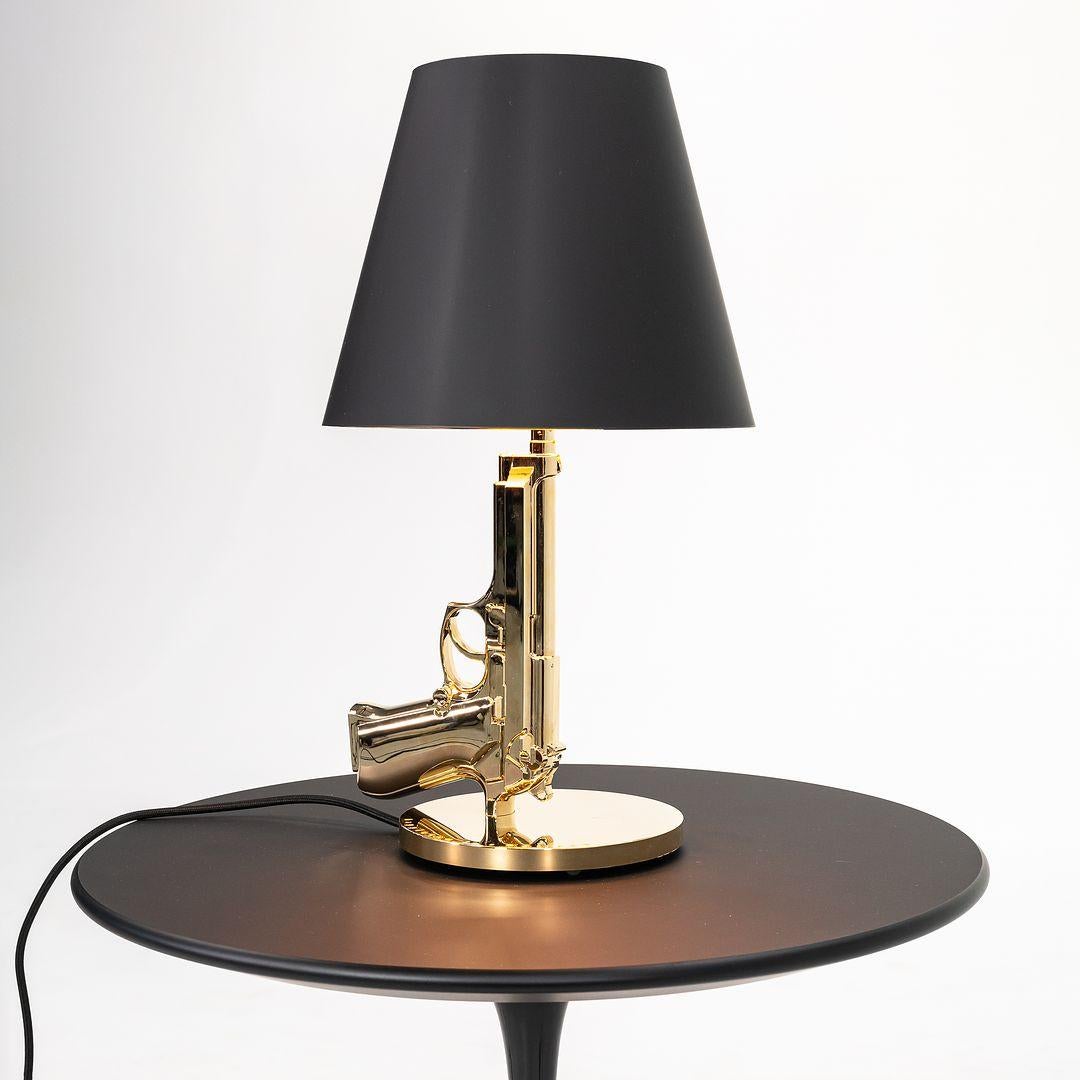 Nous proposons à la vente une lampe de chevet Gun en aluminium moulé sous pression en or 18 carats et un abat-jour en papier plastifié noir sérigraphié en or à l'intérieur. La lampe a été conçue par Philippe Starck, produite par Flos¬†en Italie et