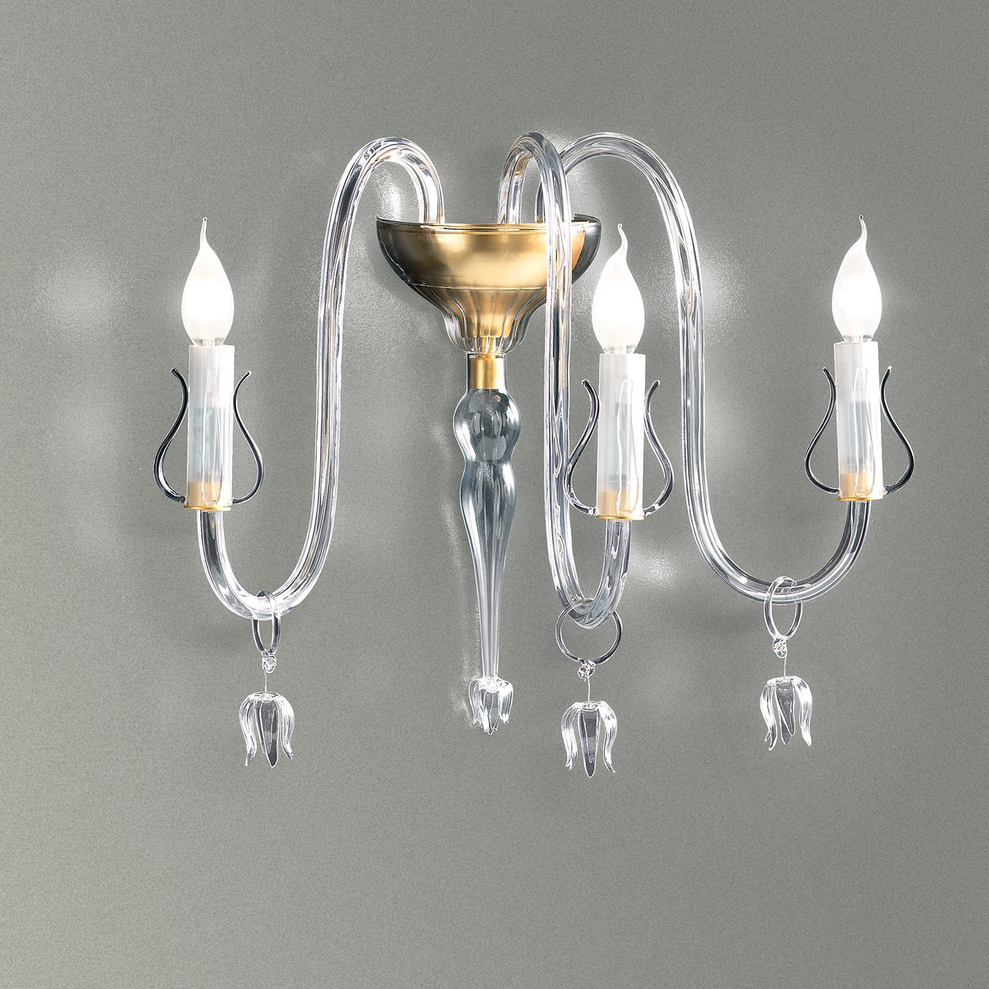 Featuring a matt gold finish on the wall attachment and three candlesticks, the main structure of this simple and delightfully elegant wall lamp is crafted in beautiful clear Murano glass and includes hanging pendants that provide an element of